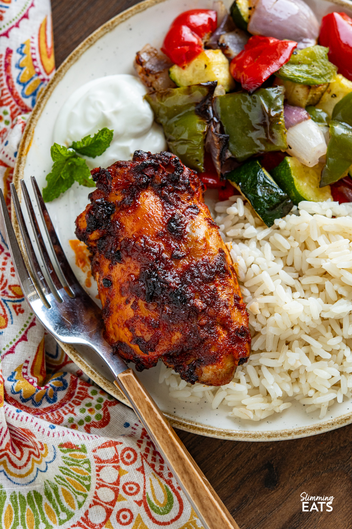 close up of Air Fryer Harissa Chicken on  white and cream plate with rice and sauteed  onion, peppers and zucchini and a dollop of yoghurt. 