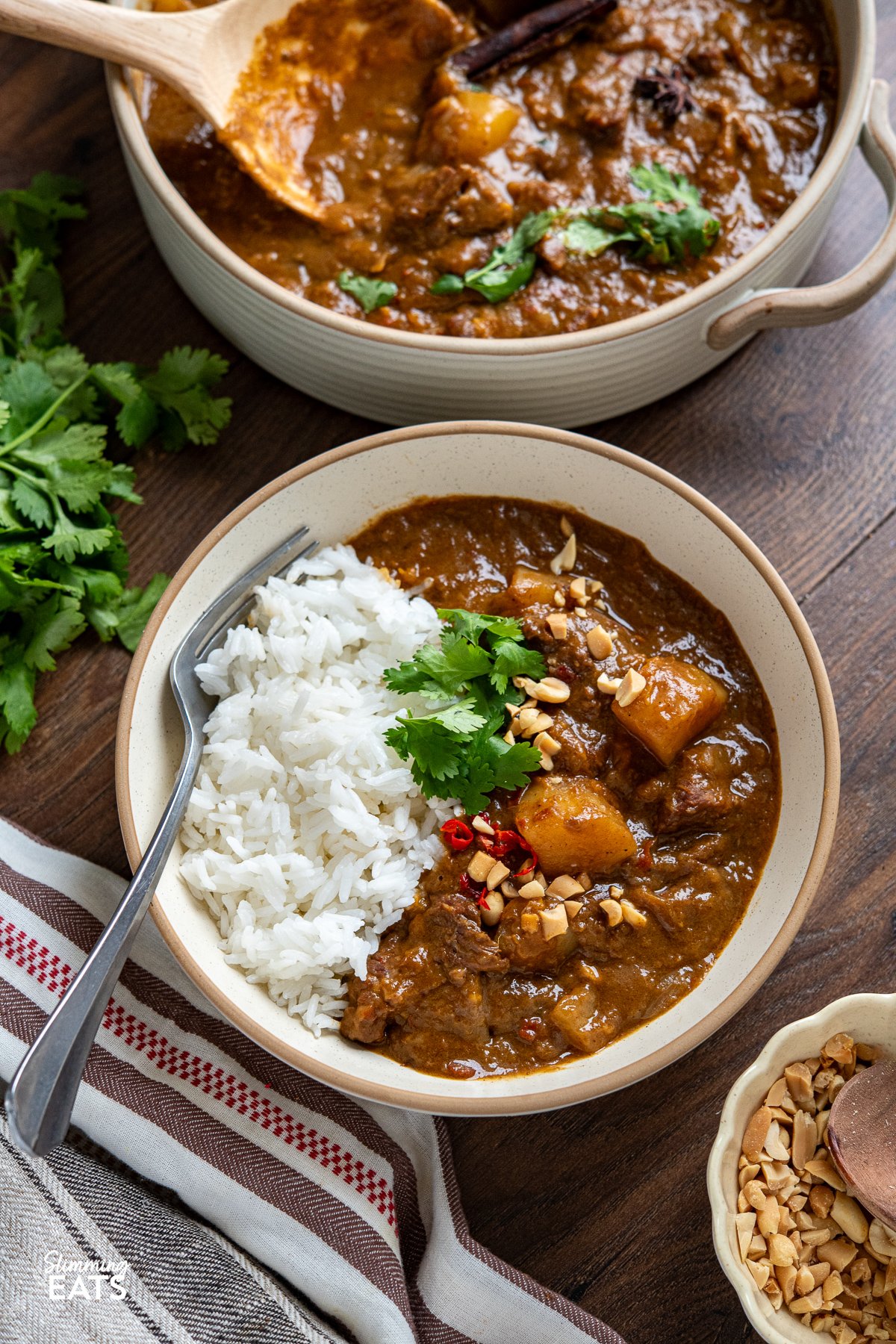 beef massaman curry in bowl with jasmine rice, coriander, and crushed peanuts