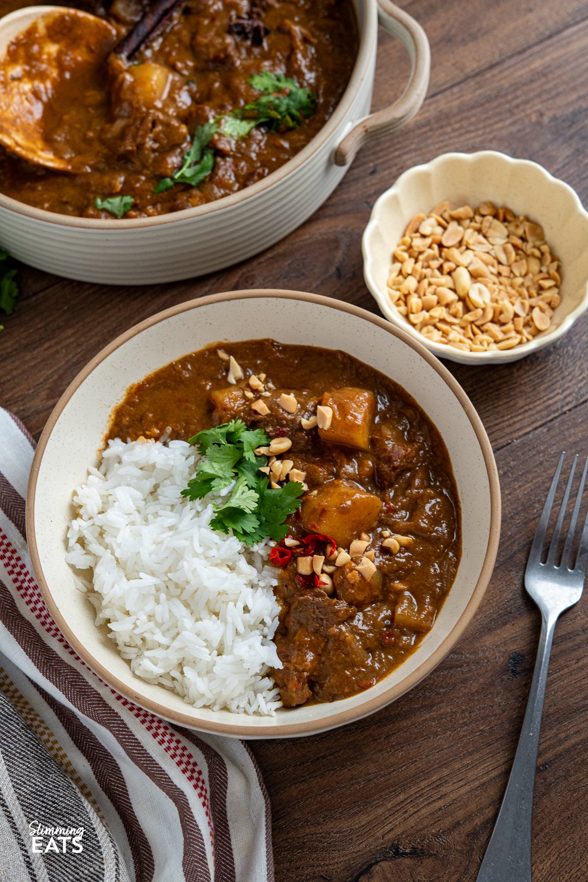 beef massaman curry in bowl with jasmine rice, coriander, and crushed peanuts