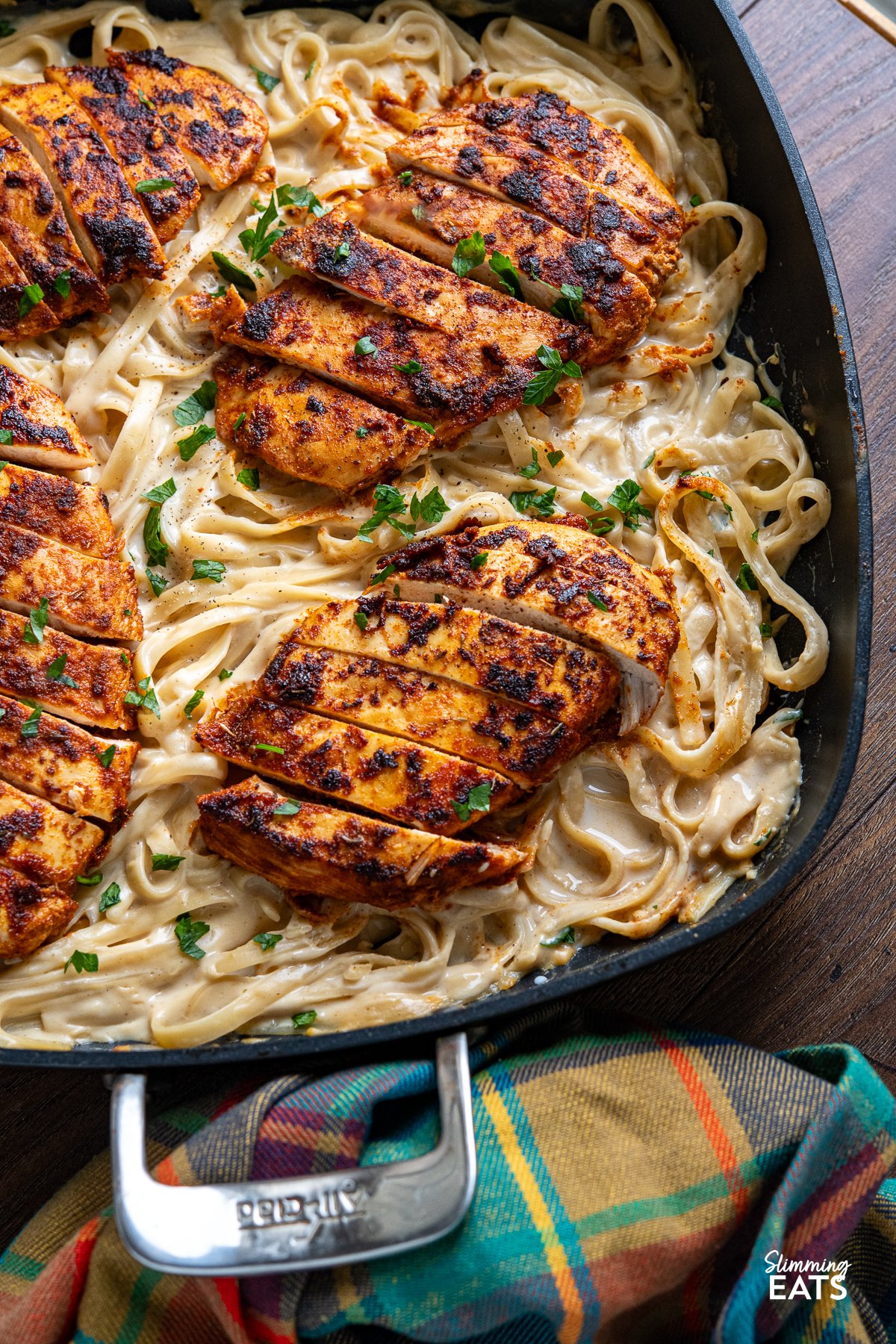 One Pot Cajun Chicken Alfredo - This mouthwatering dish features tender chicken breast seasoned to perfection with a homemade blend of bold Cajun spices, nestled into a lighter creamy Alfredo-coated fettuccine. close up of One Pot Cajun Chicken Alfredo Pasta in a square frying pan