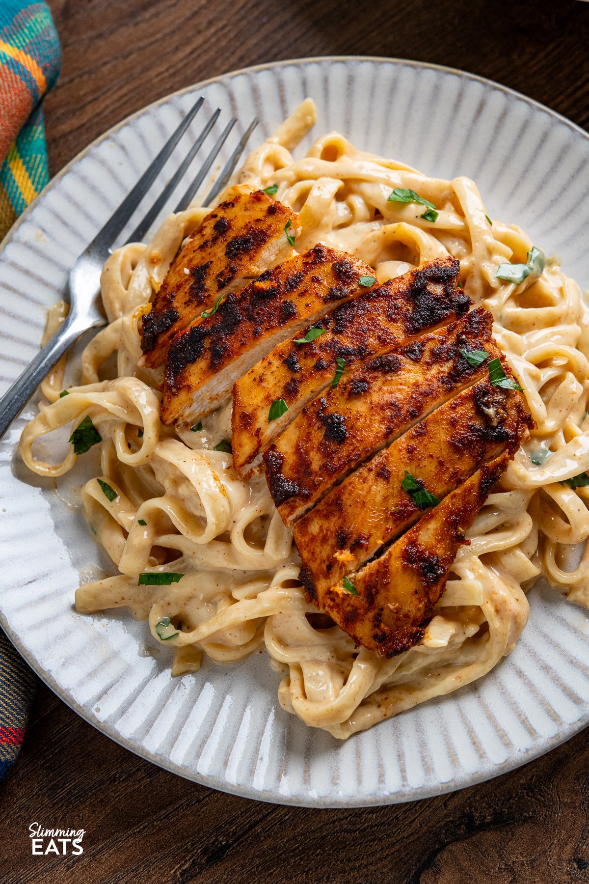 One Pot Cajun Chicken Alfredo - This mouthwatering dish features tender chicken breast seasoned to perfection with a homemade blend of bold Cajun spices, nestled into a lighter creamy Alfredo-coated fettuccine. close up of Cajun Chicken Alfredo Pasta on white plate with fork