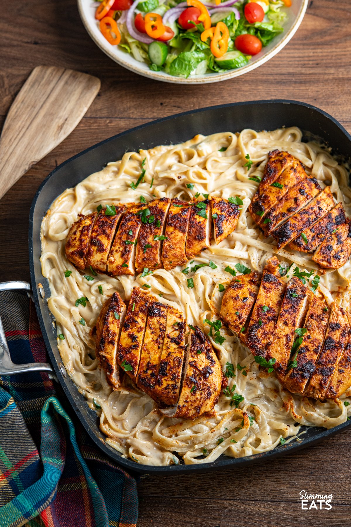 One Pot Cajun Chicken Alfredo Pasta in a square frying pan with bowl of salad above. 