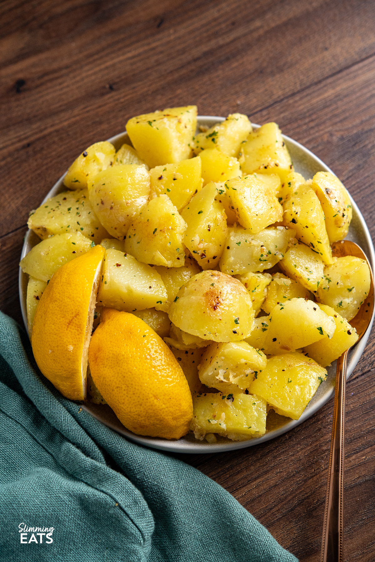 Ready to serve: Lemon garlic potatoes in a serving bowl with a spoon and lemon wedges