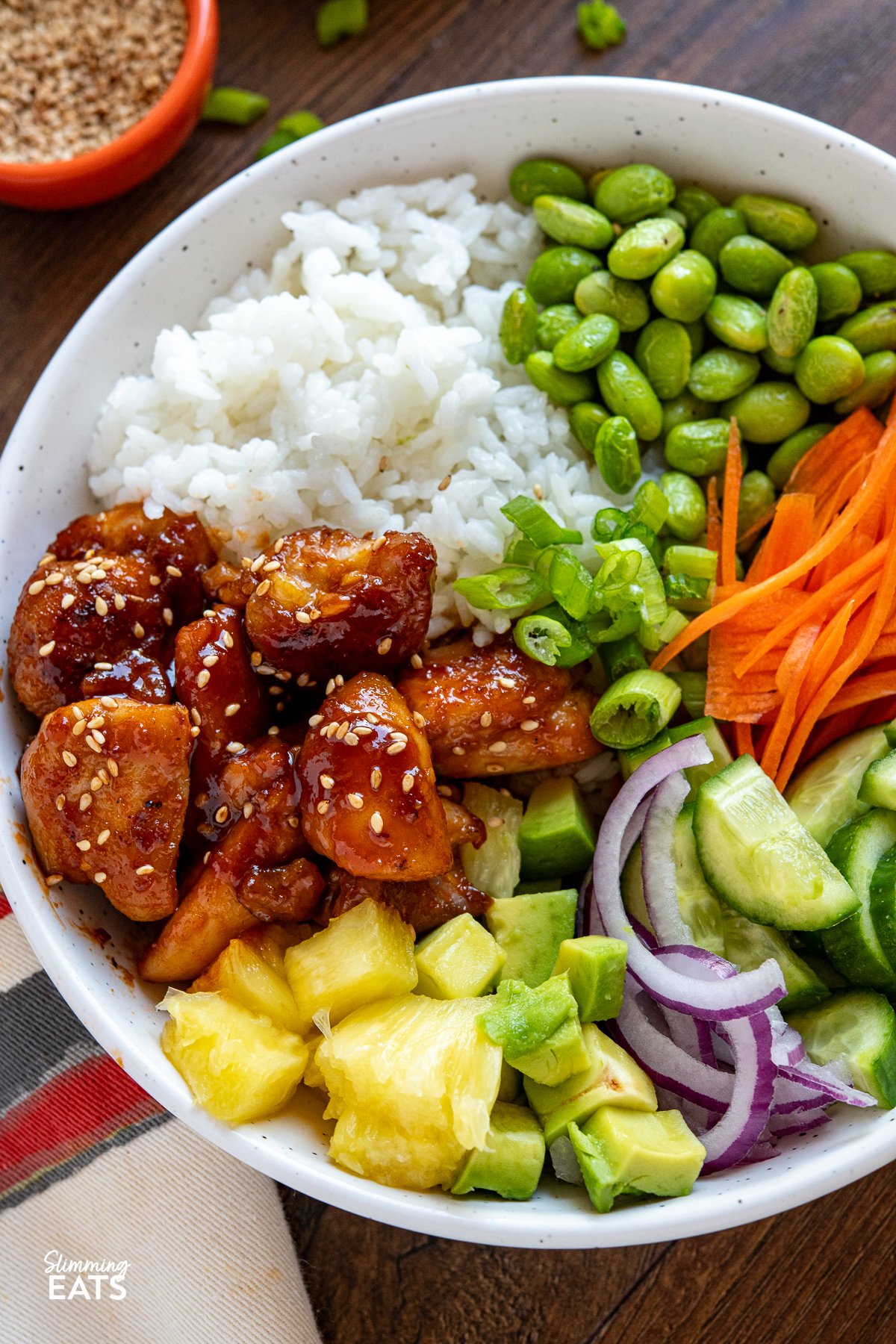 Hawaiian Chicken Poke Bowl - Bursting with freshness and vibrancy, every mouthful offers a symphony of flavours. From succulent chicken in sauce to crisp veggies, pineapple, creamy avocado, fluffy rice, and a drizzle of spicy mayo. close up of White bowl filled with Hawaiian chicken poke bowl topped with assorted fresh toppings