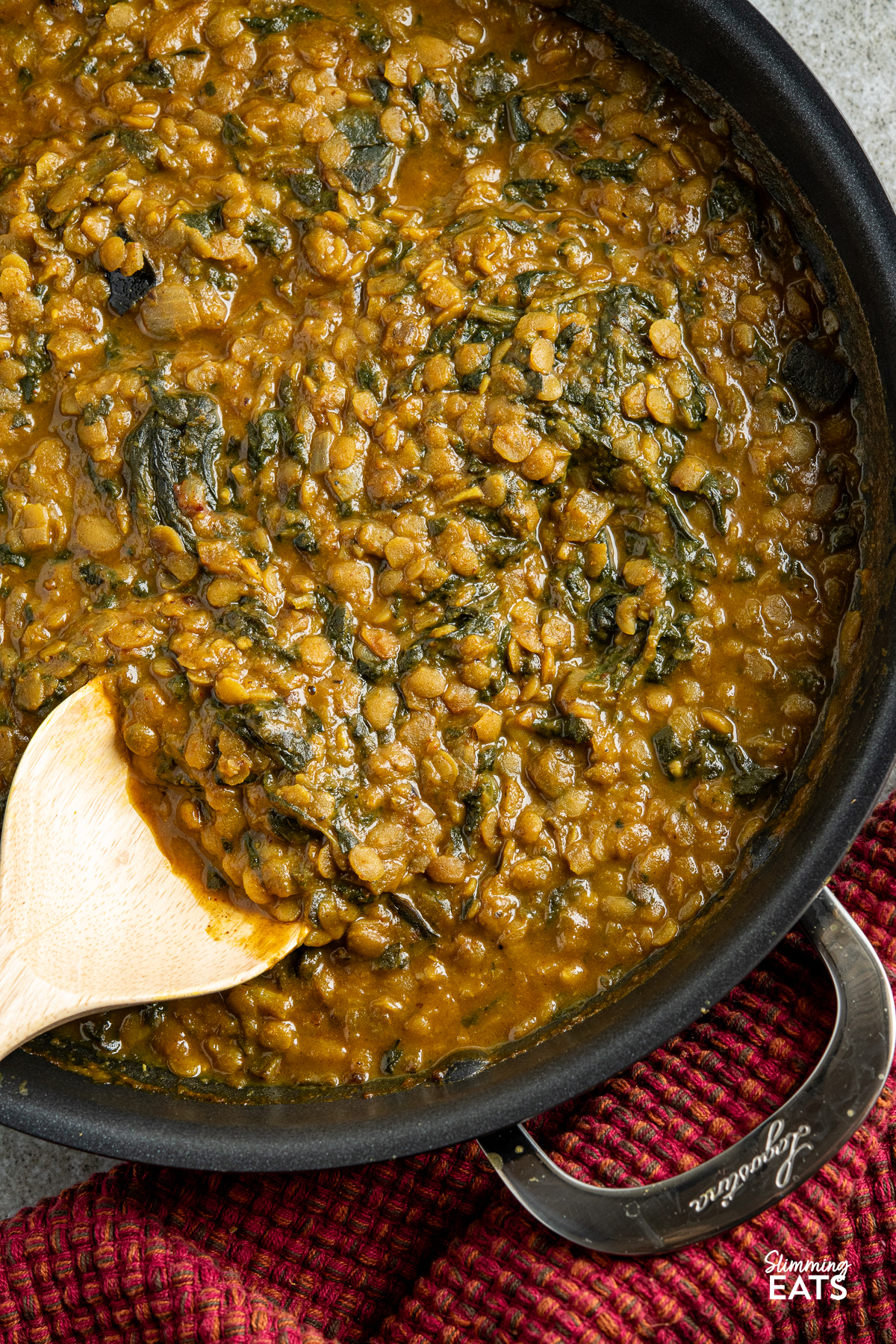 close up of Coconut, Aubergine and Spinach Dhal in a lagostina non stick pan with two handles, wooden curry spoon placed in lentils