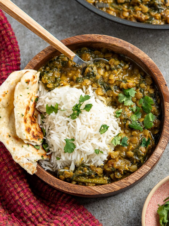 Coconut, Aubergine and Spinach Dhal served over rice with naan bread in wooden bowl, pan of dhal in background