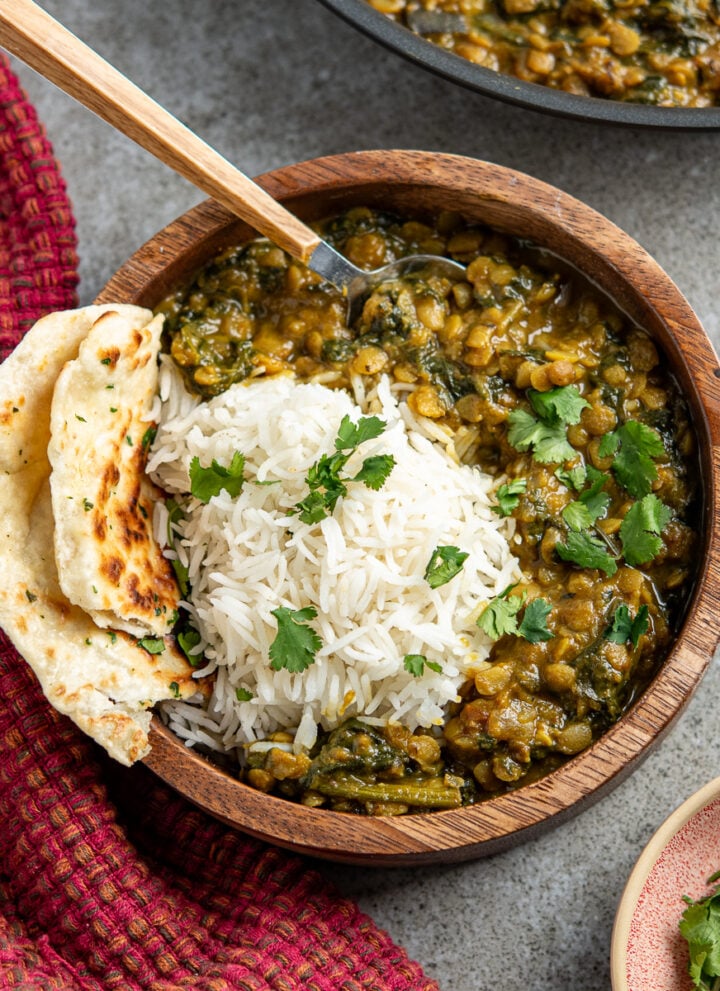 Coconut, Aubergine and Spinach Dhal served over rice with naan bread in wooden bowl, pan of dhal in background