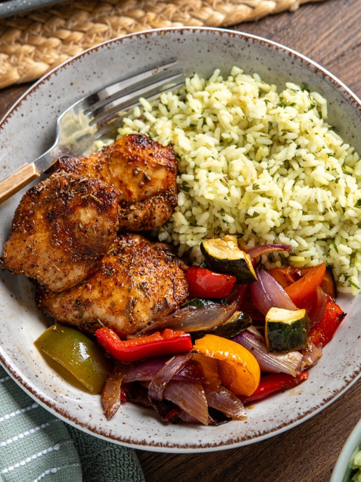 black pepper chicken, served alongside balsamic roasted vegetables and herby seasoned rice in a bowl with wooden handled fork place in left hand side of bowl
