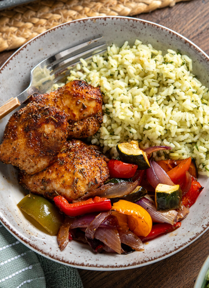black pepper chicken, served alongside balsamic roasted vegetables and herby seasoned rice in a bowl with wooden handled fork place in left hand side of bowl
