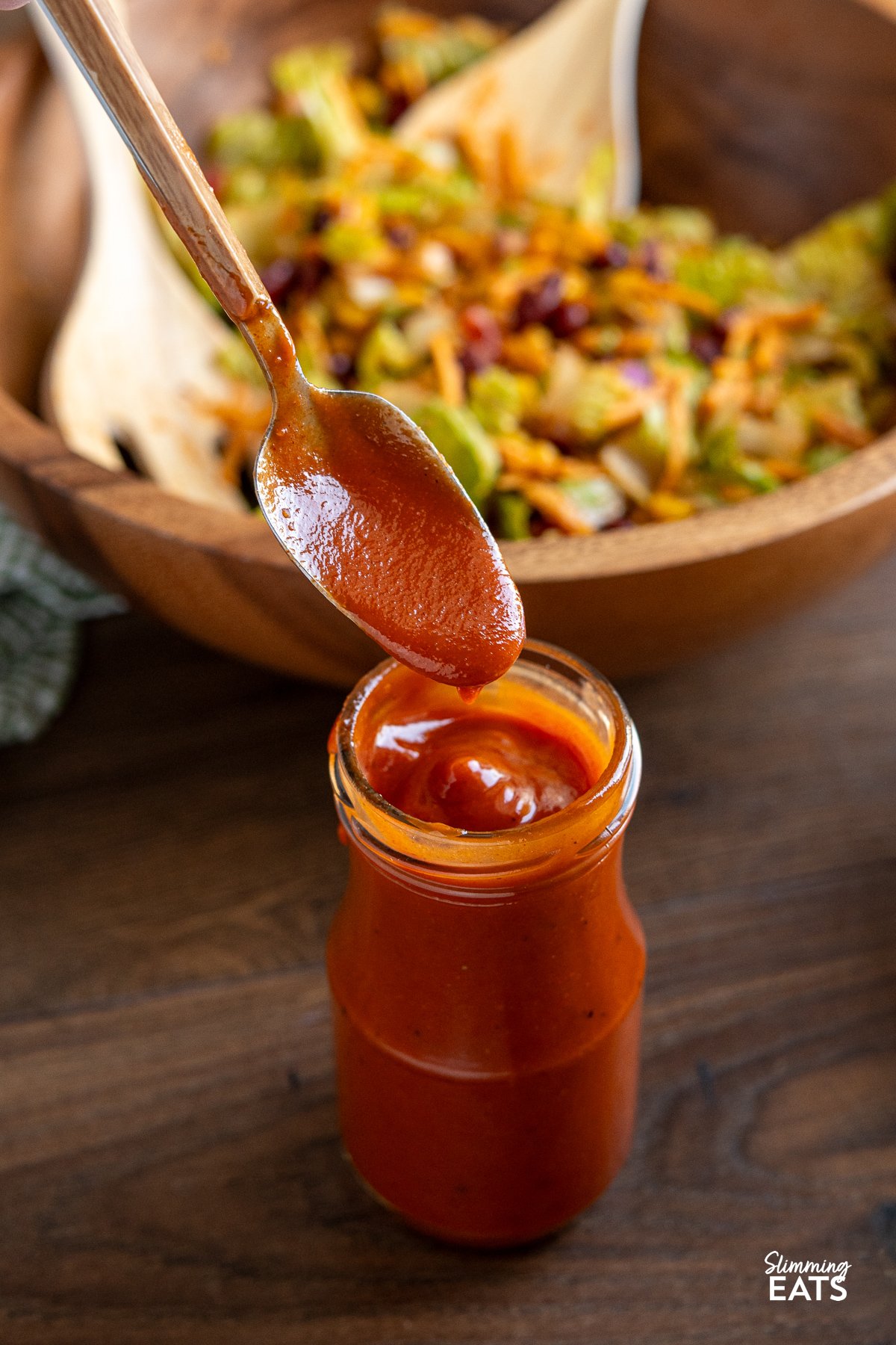 Homemade Catalina dressing being spooned from a jar, surrounded by vibrant taco salad in a wooden bowl