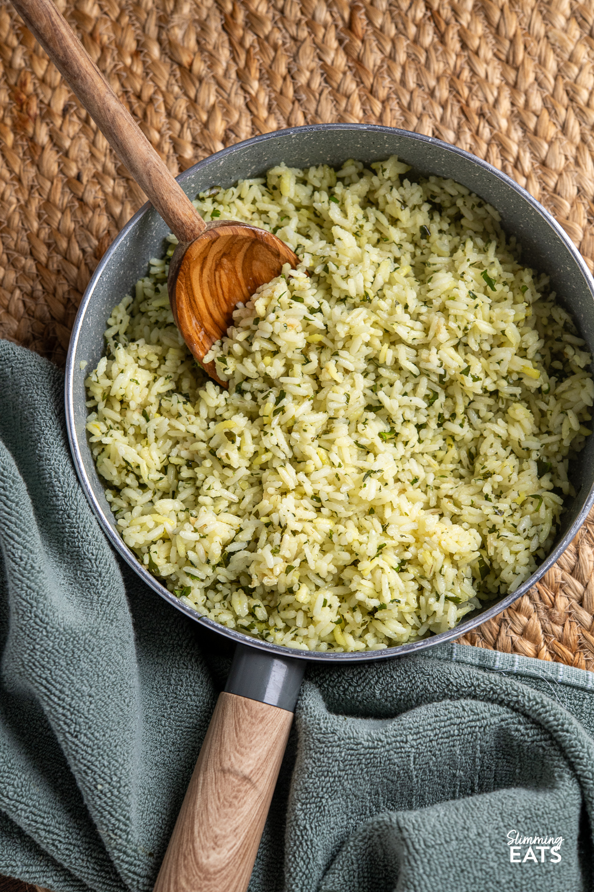 Cooked herby garlic rice in a wooden handled saucepan with olive wood spoon placed in rice.