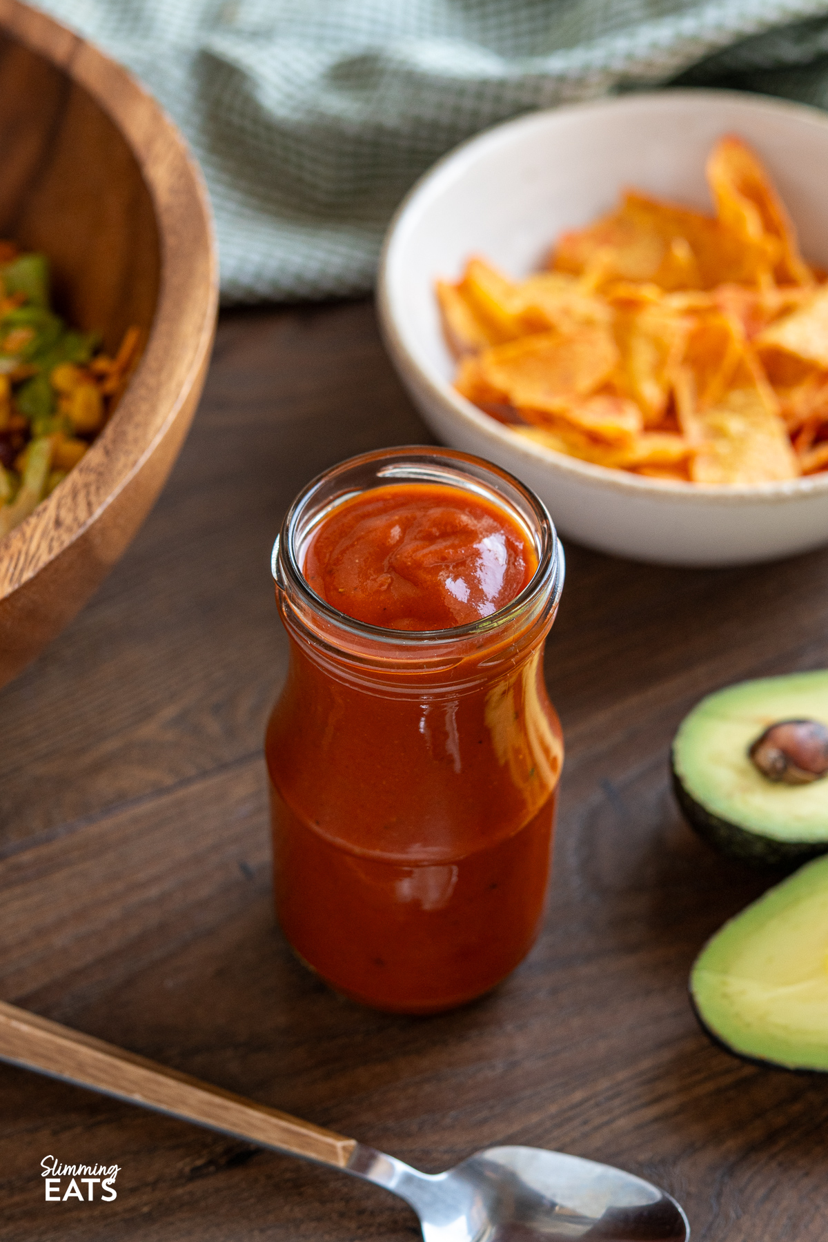 Homemade Catalina dressing in a jar, surrounded by vibrant taco salad ingredients on a wooden board, with halved avocado in the foreground.