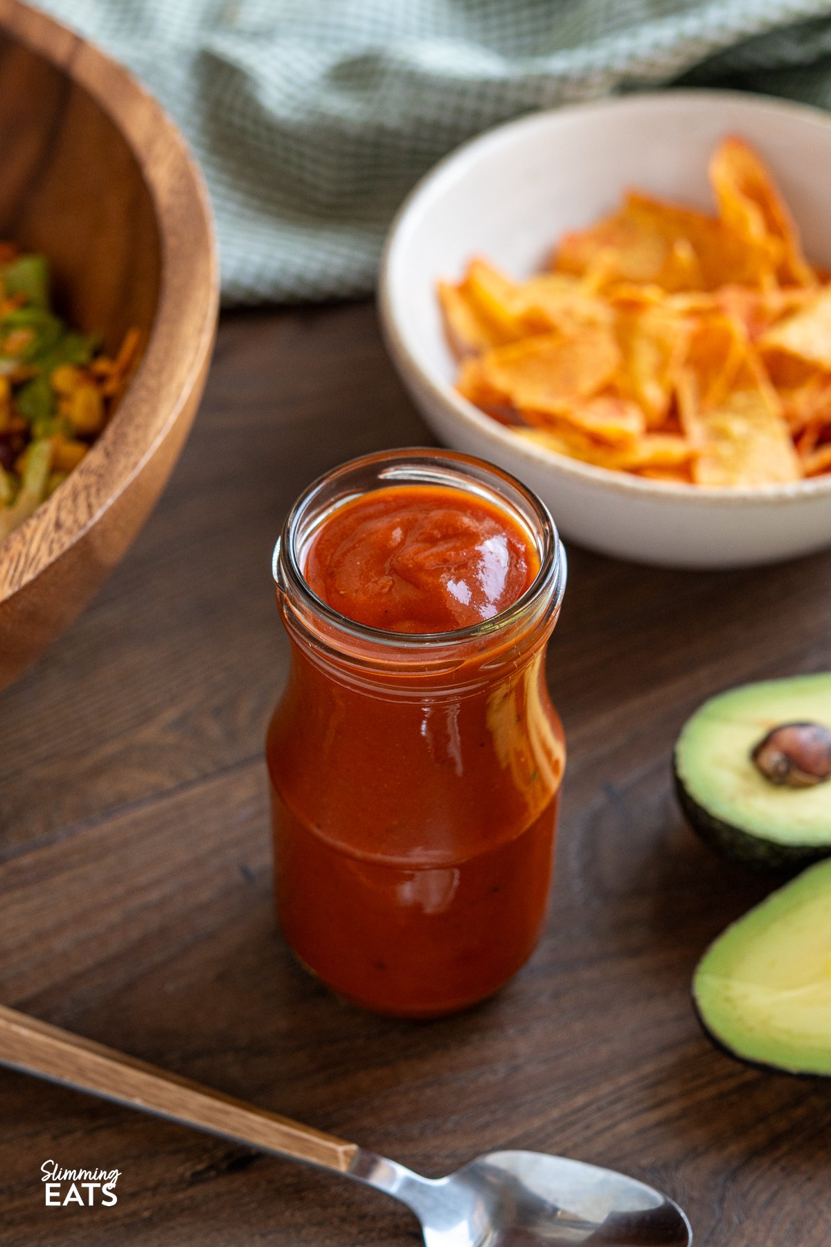 Craving a punchy, tangy dressing to jazz up your salads without the guilt? Look no further! Dive into my homemade low-calorie Catalina dressing recipe that's bursting with zest and zing. It's quick and easy to prepare, using just a few simple ingredients. Whip up a batch today and enjoy a flavourful twist on your salad. Homemade Catalina dressing in a jar, surrounded by vibrant taco salad ingredients on a wooden board, with halved avocado in the foreground.