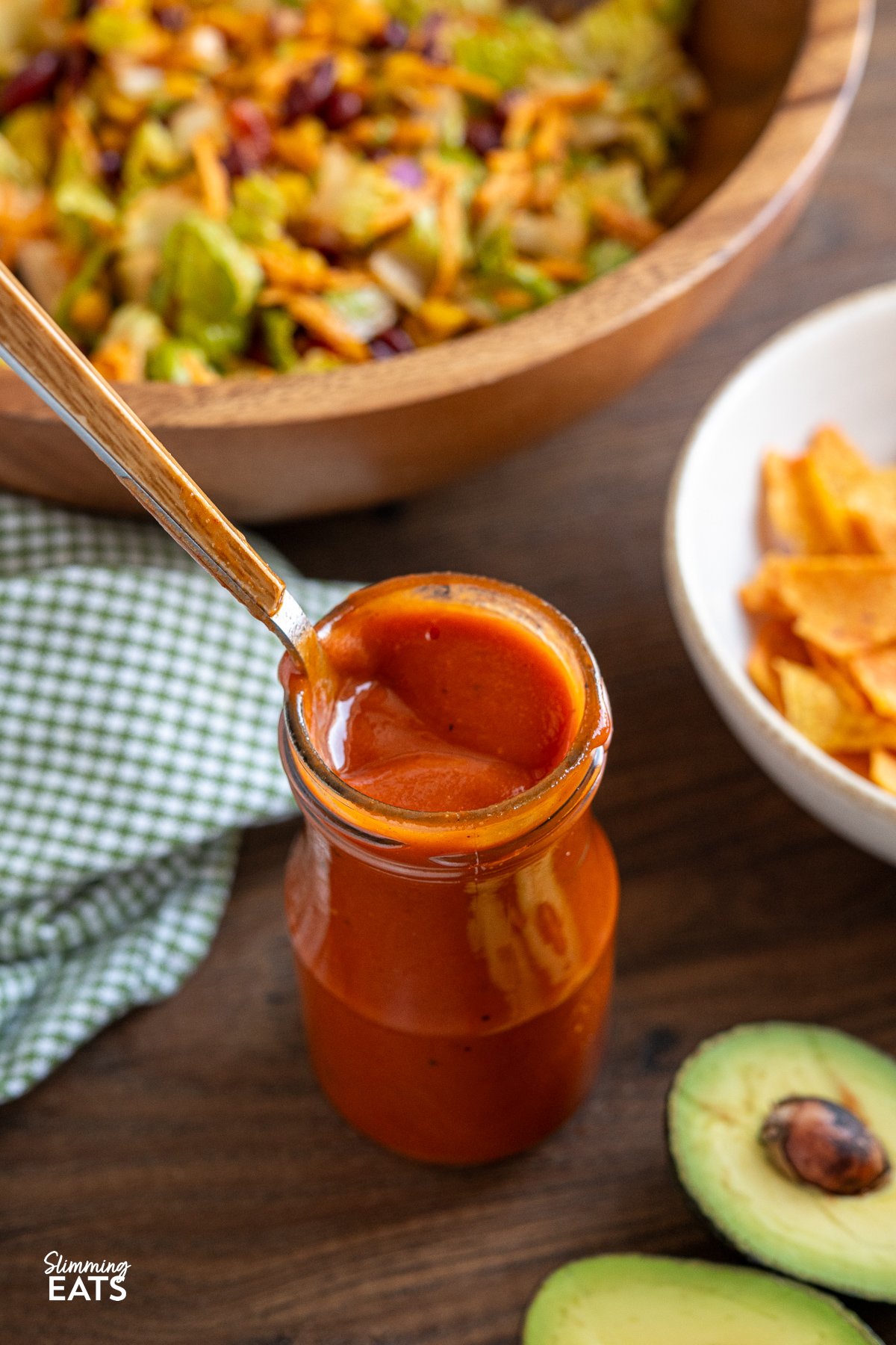 Homemade Catalina dressing being in a jar with spoon, surrounded by vibrant taco salad in a wooden bowl with halved avocado in foreground