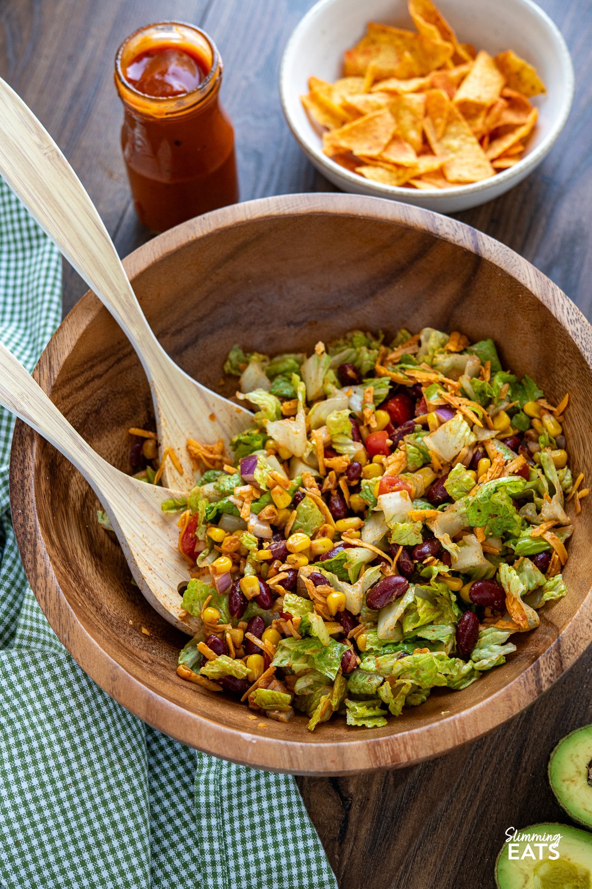 taco salad combined in a wooden bowl with salad spoon and jar of catalina dressing in background with bowl of doritos. 