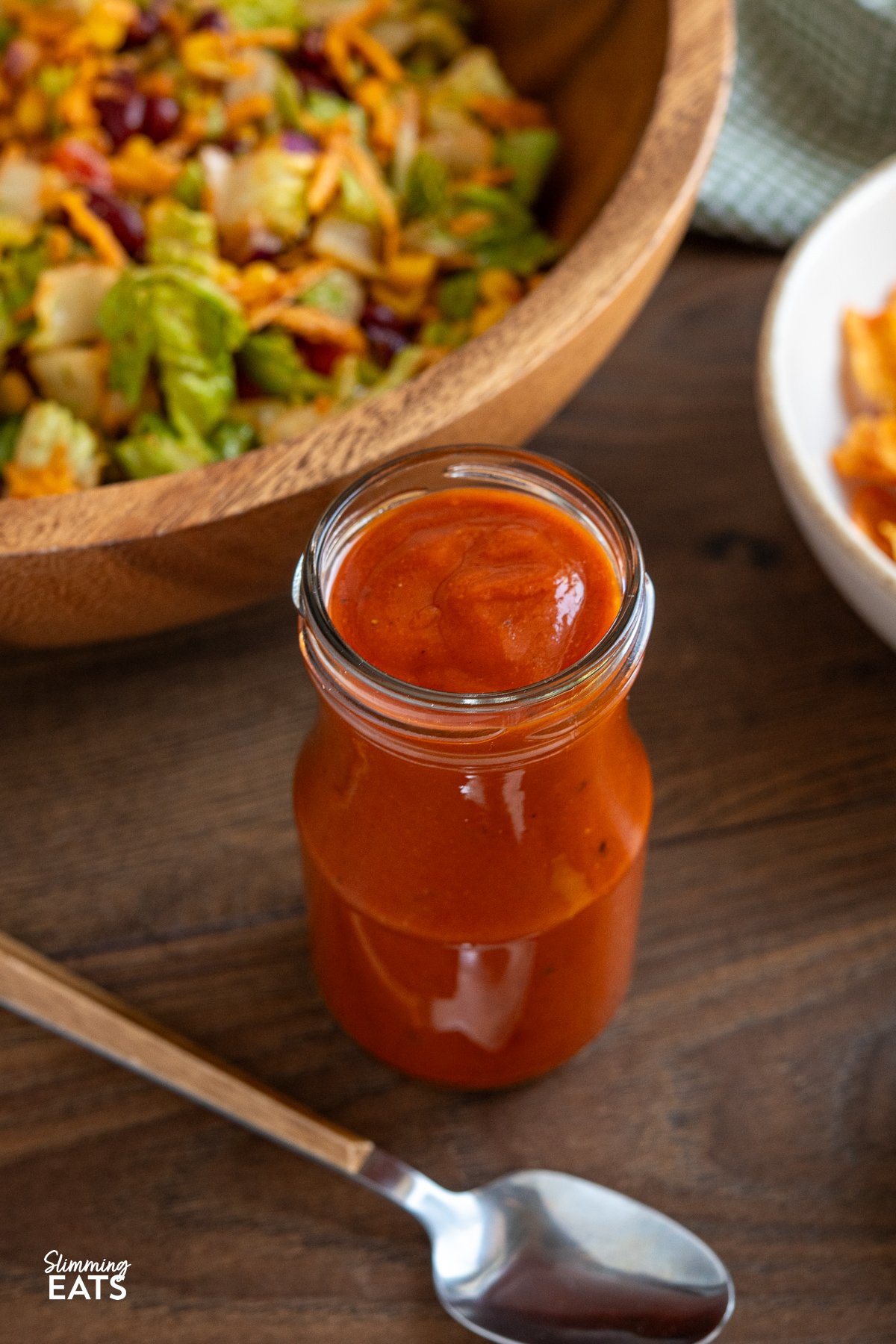 Homemade Catalina dressing in a jar, surrounded by vibrant taco salad ingredients on a wooden board, with halved avocado in the foreground.