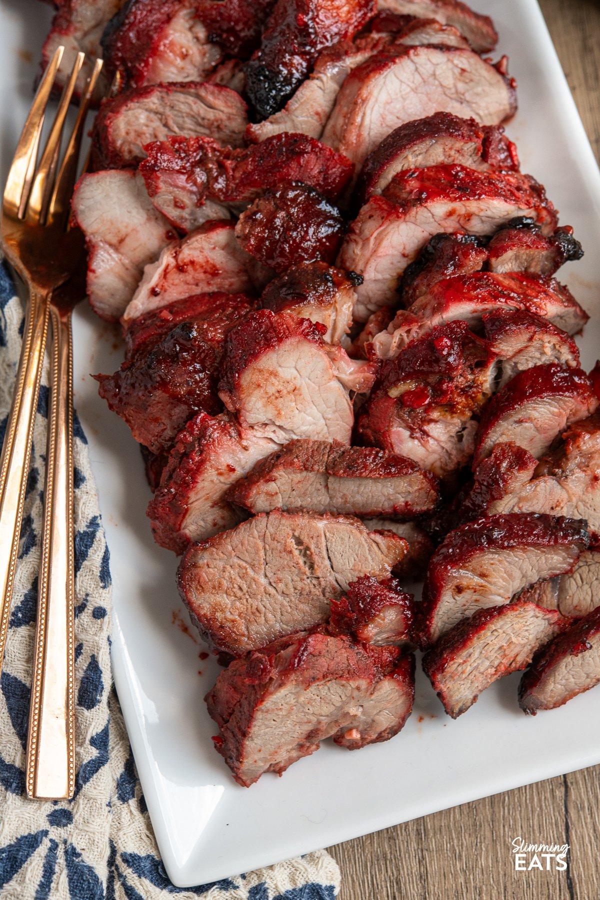Easy Make-at-Home Char Siu Pork - Tender slices of pork, baked to perfection in the oven, are infused with the rich, tantalising flavours of the Chinese-style BBQ marinade. close up of Sliced Char Siu Pork arranged on a white rectangular plate with two forks placed on the side.