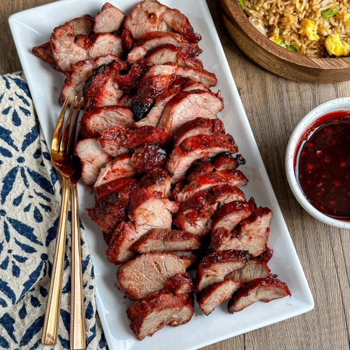 char sui pork sliced on a plate with bowl of egg fried rice and extra sauce on side