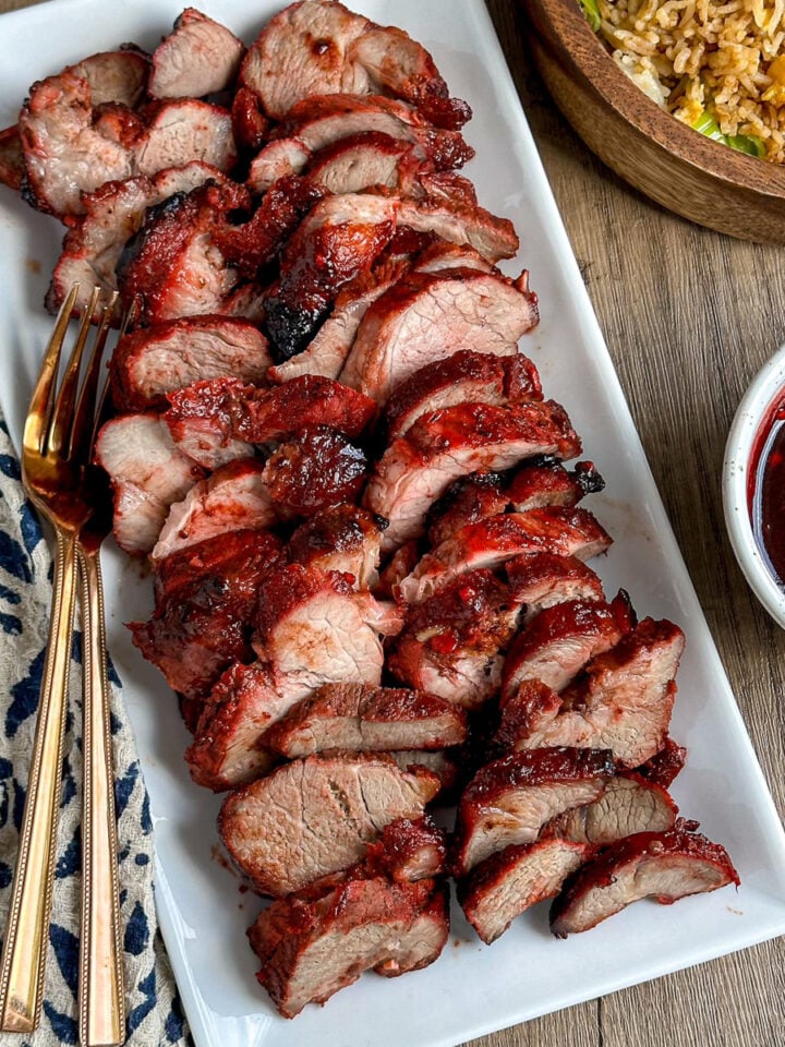 char sui pork sliced on a plate with bowl of egg fried rice and extra sauce on side