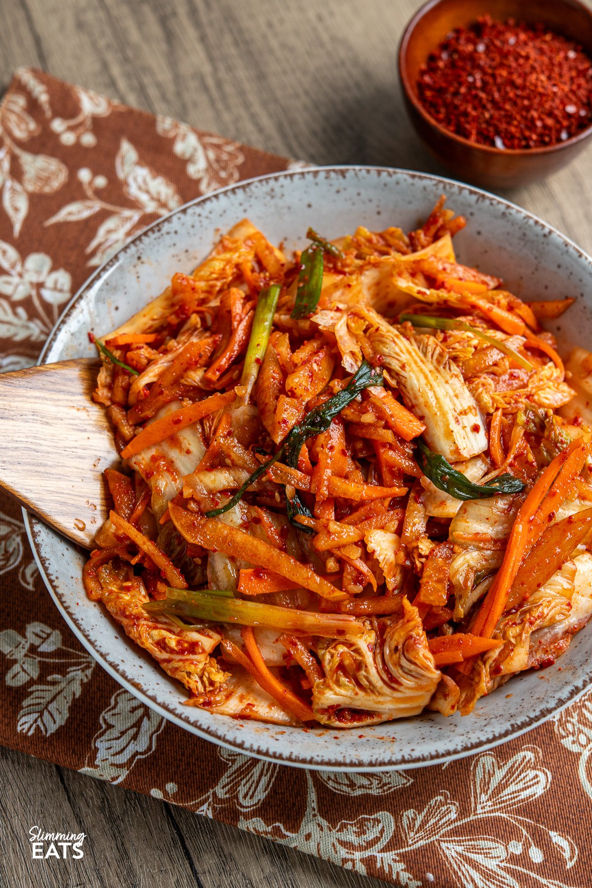 Looking to add a burst of vibrant flavour to your meals without the strong tang of traditional fermented kimchi? This quick and easy fresh kimchi recipe is the perfect introduction. By skipping the fermentation process, you get a crunchy, refreshing side dish that pairs wonderfully with all your favourite Korean dishes. Made with crisp napa cabbage, crunchy carrots, green onions, and sweet Asian pear, this delightful kimchi offers a spicy yet lightly sweet taste that will soon become a staple at your table. quick fresh kimchi freshly prepared in a large bowl with wooden spoon place in kimchi