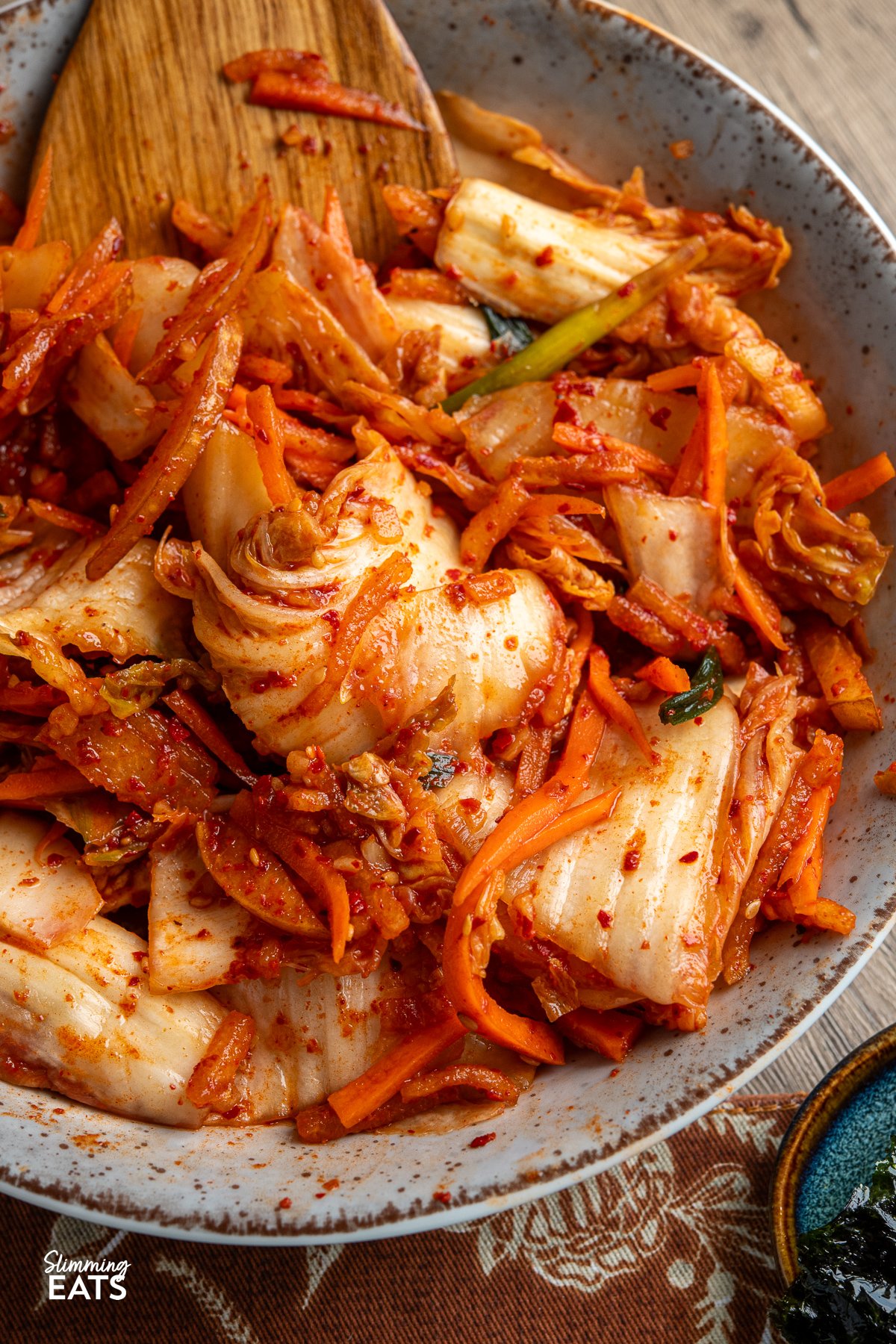 Looking to add a burst of vibrant flavour to your meals without the strong tang of traditional fermented kimchi? This quick and easy fresh kimchi recipe is the perfect introduction. By skipping the fermentation process, you get a crunchy, refreshing side dish that pairs wonderfully with all your favourite Korean dishes. Made with crisp napa cabbage, crunchy carrots, green onions, and sweet Asian pear, this delightful kimchi offers a spicy yet lightly sweet taste that will soon become a staple at your table. quick fresh kimchi freshly prepared in a large bowl with wooden spoon place in kimchi