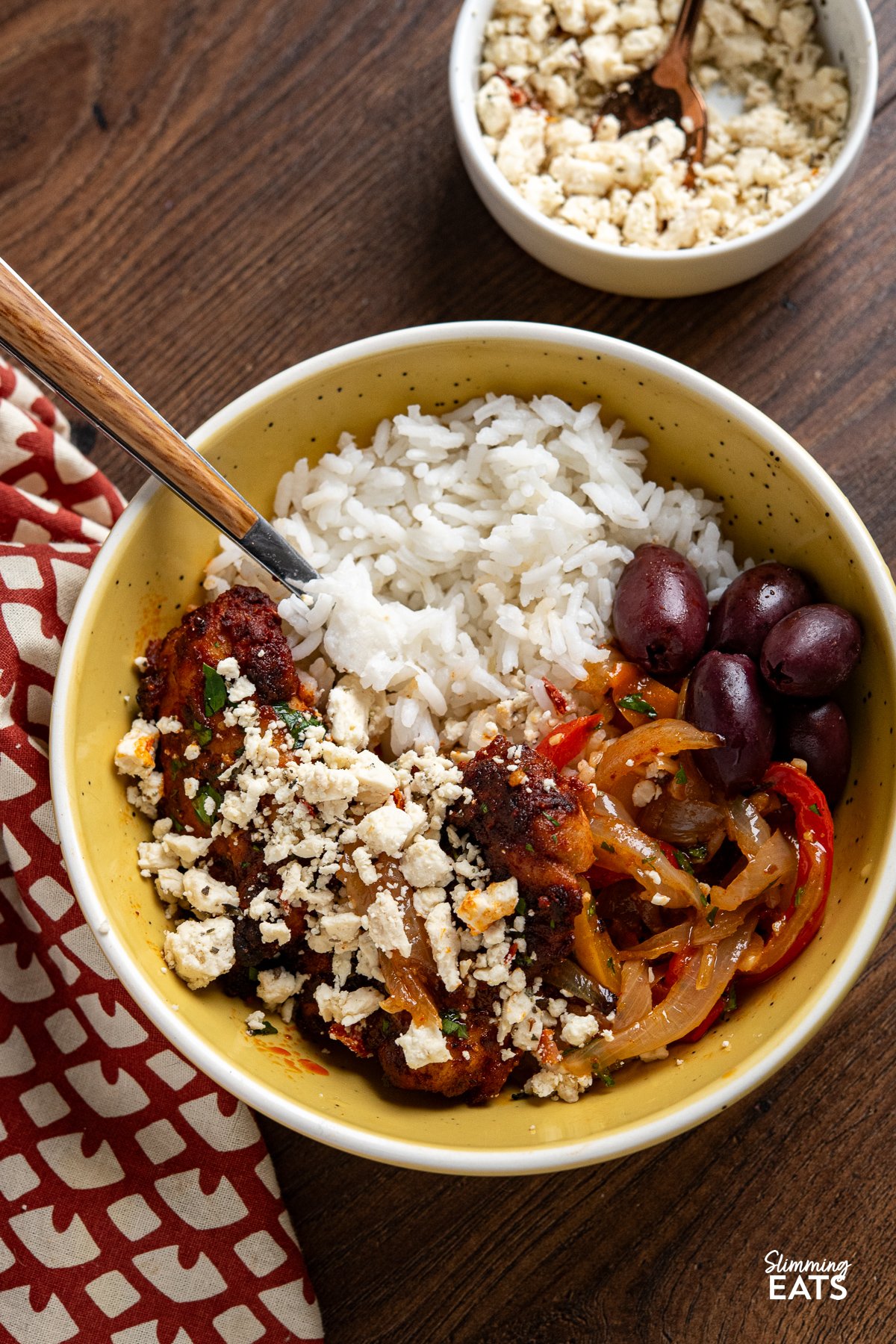 seasoned baked chicken thighs on a sheet pan with roasted juicy peppers in a yellow bowl with rice and kalamata olives and crumbled feta.