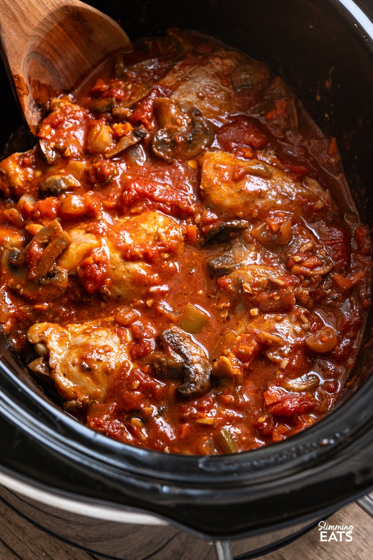 Transform your family meals with Slow Cooker Chicken Cacciatore. Tender chicken thighs meld beautifully with green bell pepper and mushrooms in a rich tomato sauce. Serve it with your favourite sides for a great meal that everyone will enjoy. chicken cacciatore in slow cooker with wooden spoon