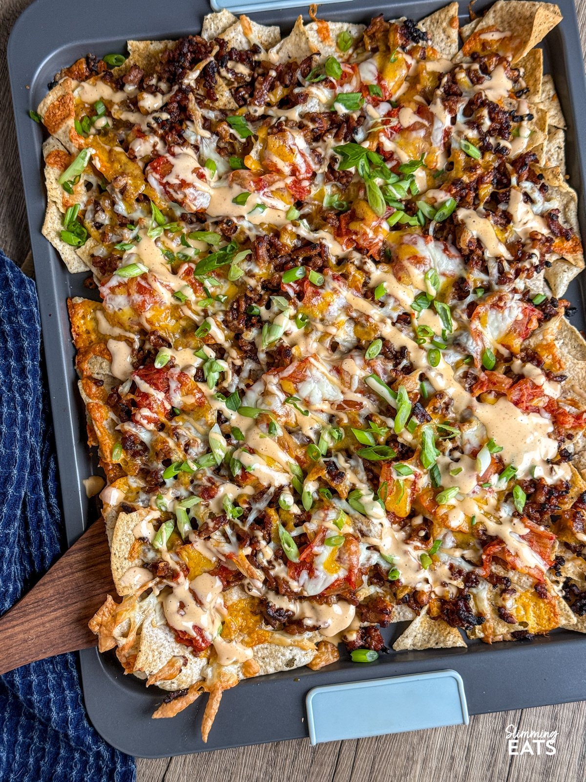 Gochujang Ground Pork Nachos with Kimchi on a non stick baking sheet with wooden spatula