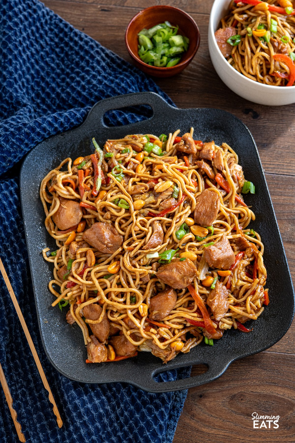 Skip the takeaway—this slow cooker chicken noodles in oyster sauce is an easy, flavour-packed dinner. Tender chicken simmers in a rich, savoury sauce with garlic, ginger, and oyster sauce, creating the perfect base for soft, slurp-worthy noodles and colourful veggies. chicken noodles in oyster sauce with peanuts all served up on a black double handled square plate, serving visible to edge of picture in a bowl.