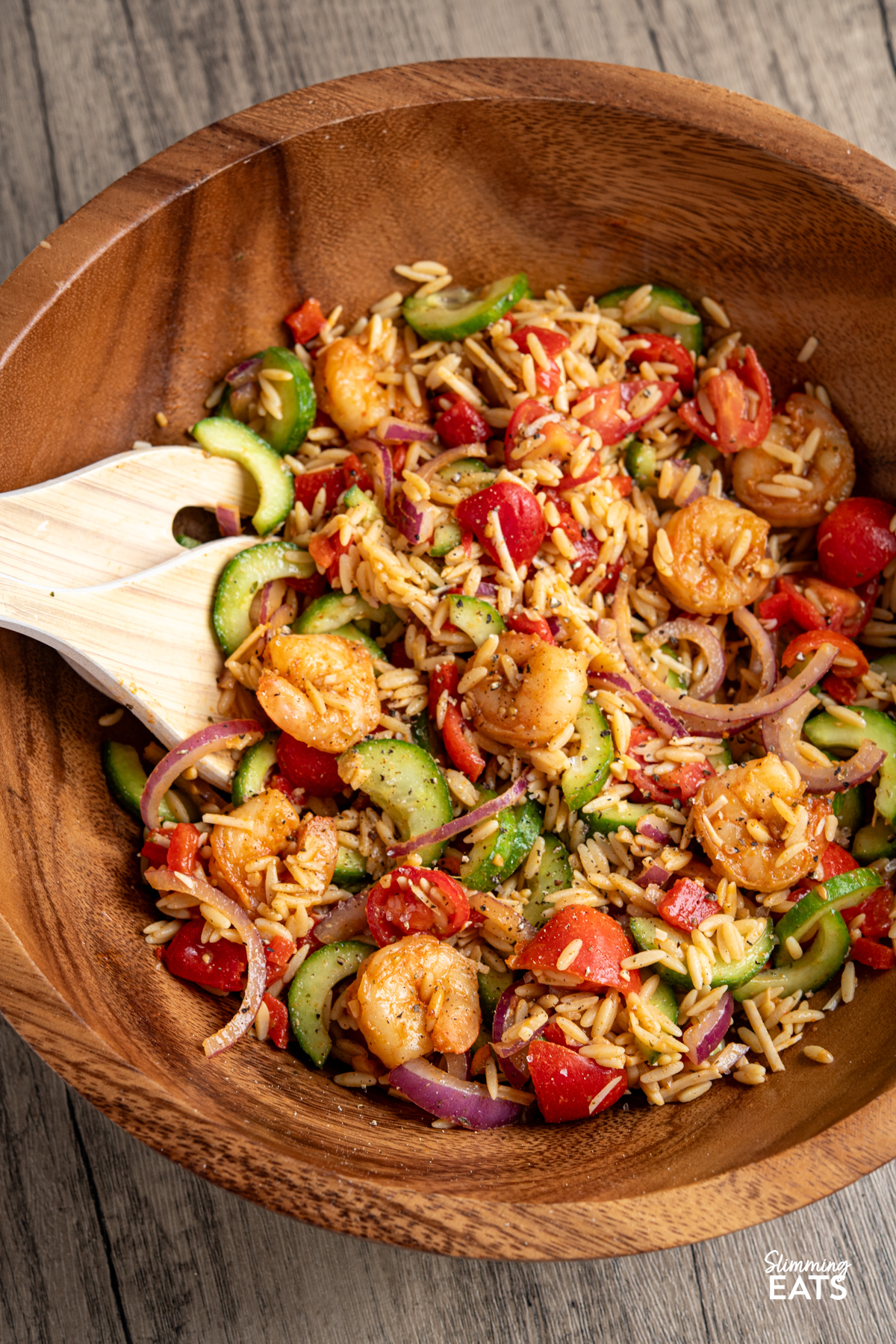Fresh, vibrant, and packed with flavour—this Shrimp Orzo Salad is a summer stunner. Tender orzo tossed with crisp cucumber, juicy cherry tomatoes, and slivers of red onion forms the perfect base for buttery prawns, pan-fried with garlic, parsley, paprika and a hint of chilli. A drizzle of honey, a squeeze of lime, and a generous grating of Parmesan tie it all together with a sweet-savoury kick. Easy Shrimp Orzo Salad in a wooden salad bowl with salad spoons