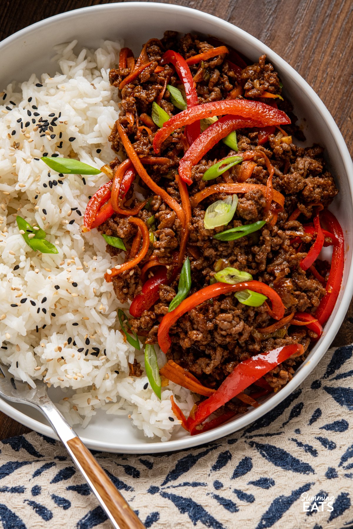 Sweet, savoury, and just the right amount of heat—this Spicy Sticky Ground Beef is a flavour-packed, fuss-free dish. Minced beef is browned and simmered in a glossy sauce of soy, sriracha, maple syrup, and sweet chilli, with garlic and ginger adding warmth. Red bell pepper and carrot bring a hint of sweetness and a satisfying bite, making every mouthful rich, sticky, and completely irresistible. close up of Spicy Sticky Ground Beef with jasmine rice in white bowl