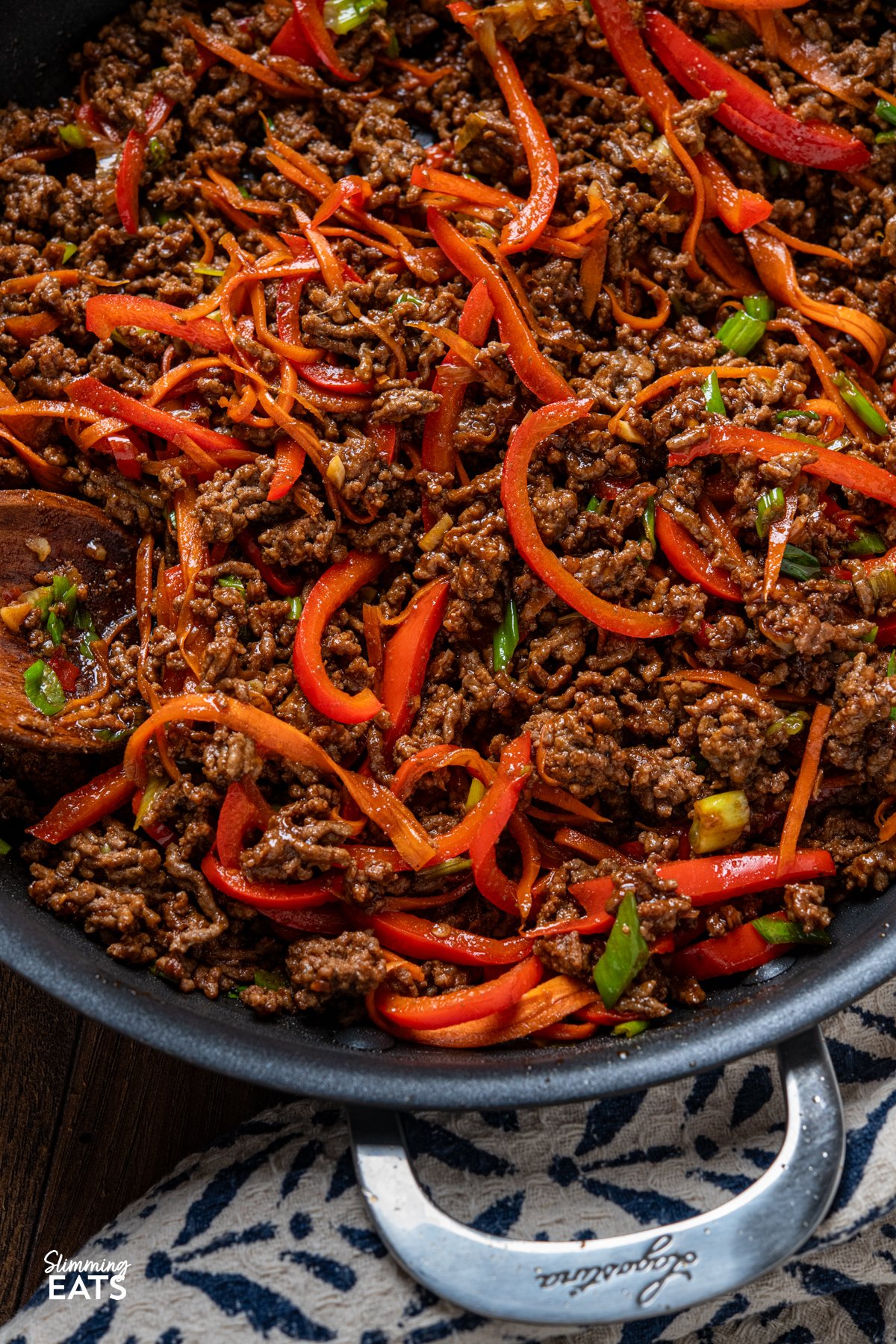 Sweet, savoury, and just the right amount of heat—this Spicy Sticky Ground Beef is a flavour-packed, fuss-free dish. Minced beef is browned and simmered in a glossy sauce of soy, sriracha, maple syrup, and sweet chilli, with garlic and ginger adding warmth. Red bell pepper and carrot bring a hint of sweetness and a satisfying bite, making every mouthful rich, sticky, and completely irresistible. close up of Spicy Sticky Ground Beef in non stick double handled skillet