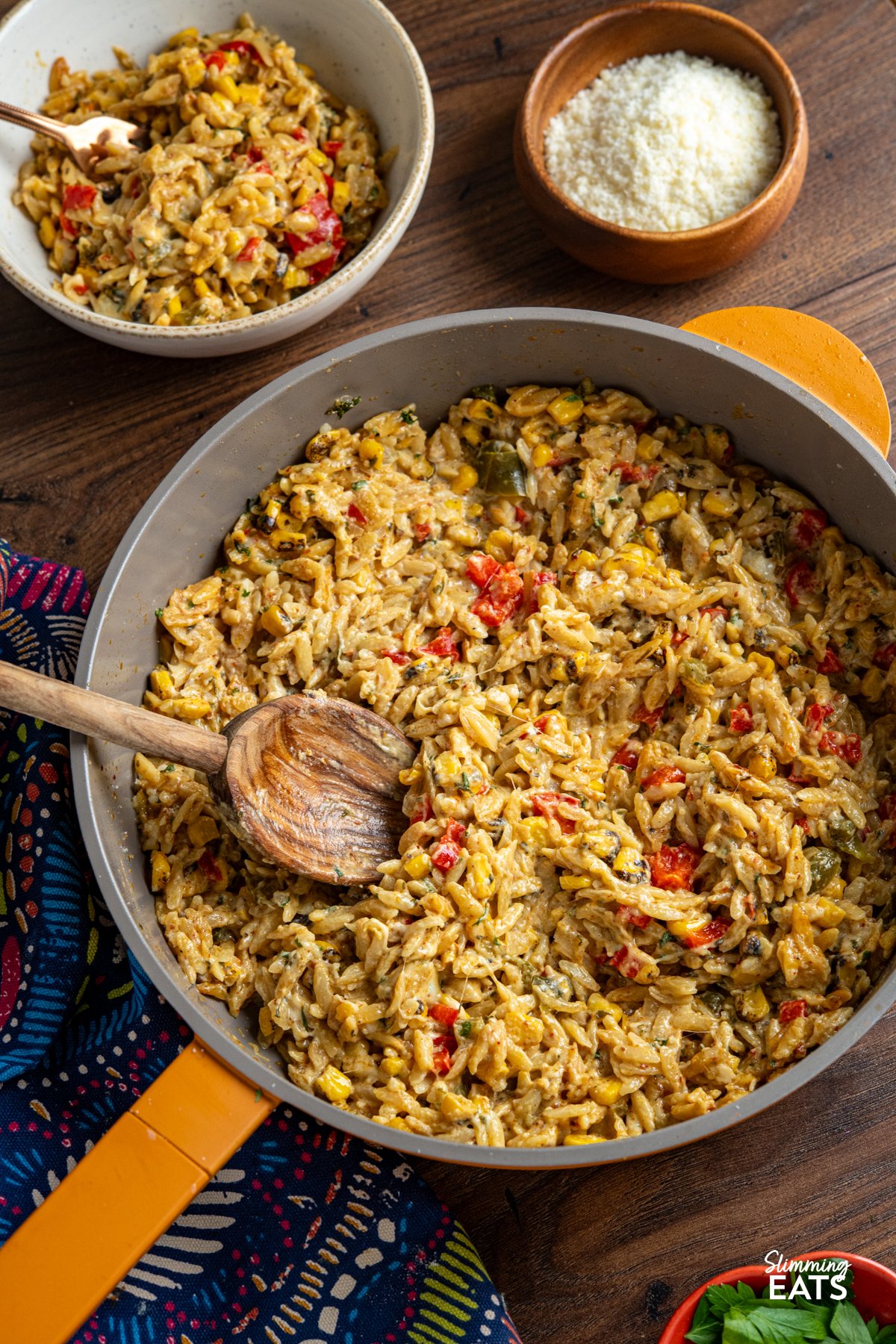 This One Pot Creamy Cheesy Spicy Corn Orzo is the kind of throw-together dinner that tastes like you put in way more effort than you actually did. It starts with smoky charred corn—bringing a hit of sweetness and depth—then builds into a cosy, creamy dish with just enough heat to keep things interesting. Think mac and cheese meets chilli-spiked corn chowder. One Pot Creamy Cheesy Spicy Corn Orzo served in a yellow non-stick skillet, with a portion in a small bowl nearby and grated Parmesan in a small wooden bowl on the side.