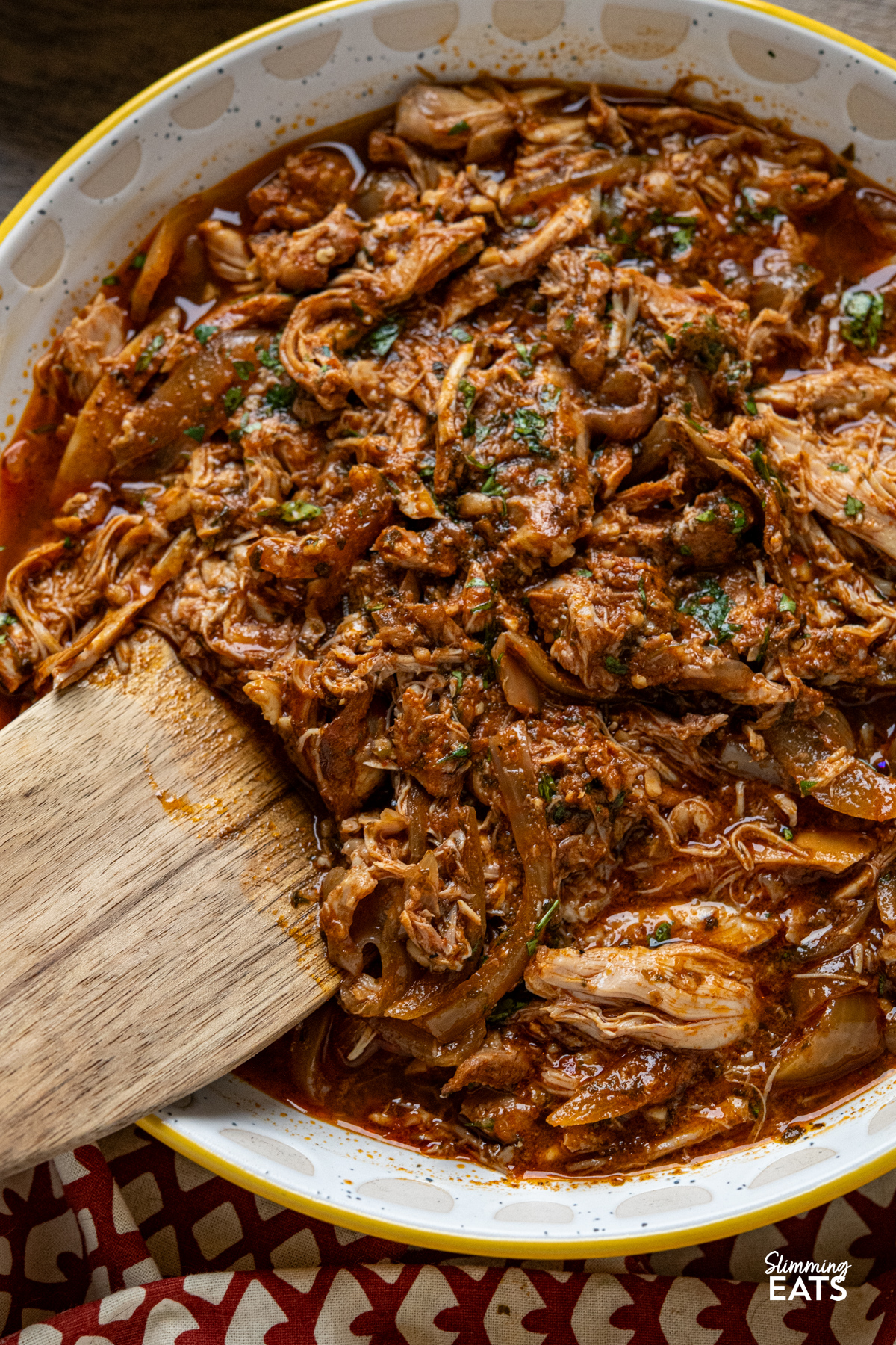 close up of Easy Slow Cooker Peri Peri Chicken in a bowl with wooden spatula 