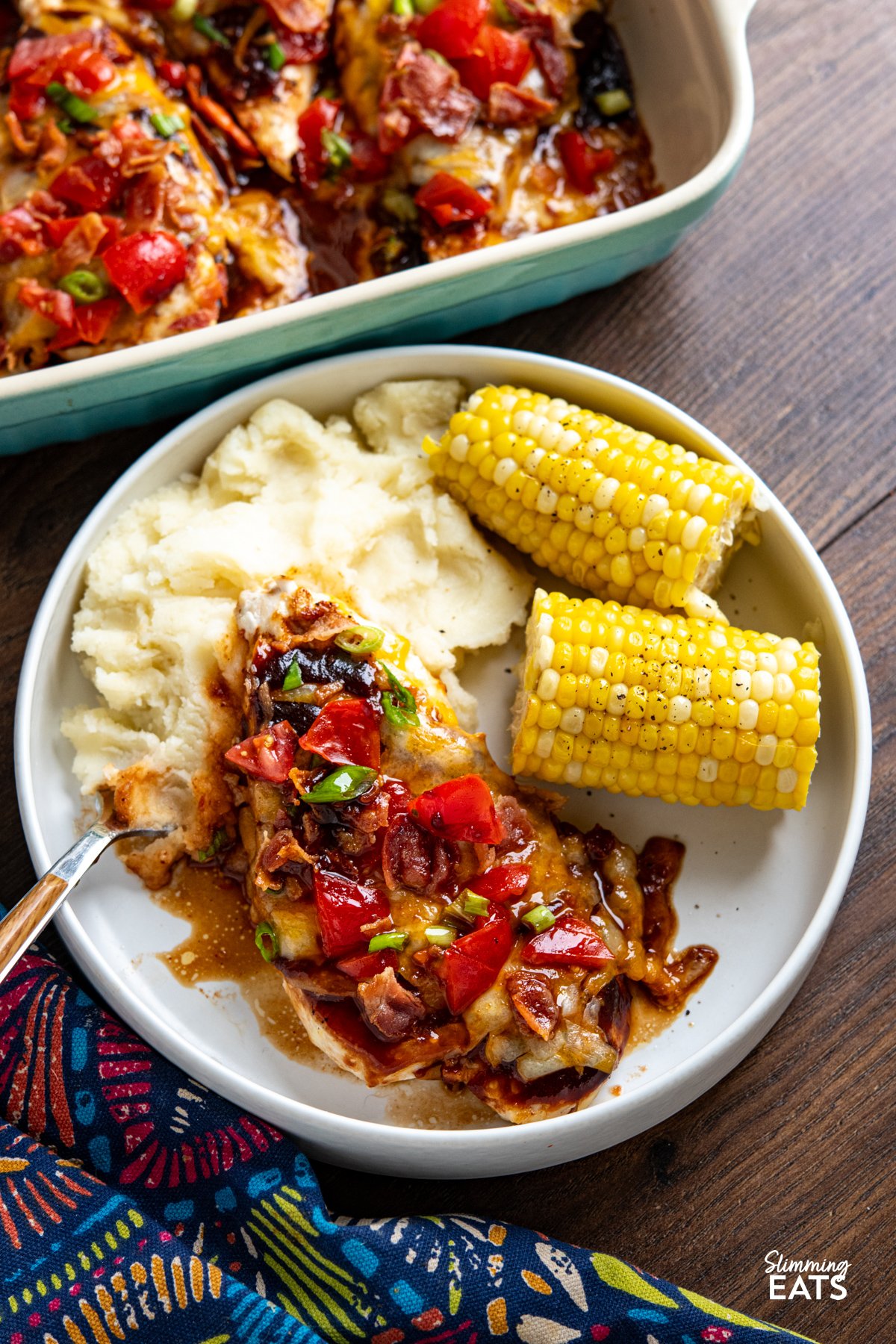 This easy Monterey Chicken is loaded with flavour, featuring tender chicken breasts topped with smoky BBQ sauce, melted cheese, fresh tomatoes and crispy bacon for a fuss-free dinner the whole family will love. white plate of Monterey Chicken served with mashed potatoes and corn on the cob, baking dish with chicken visible.