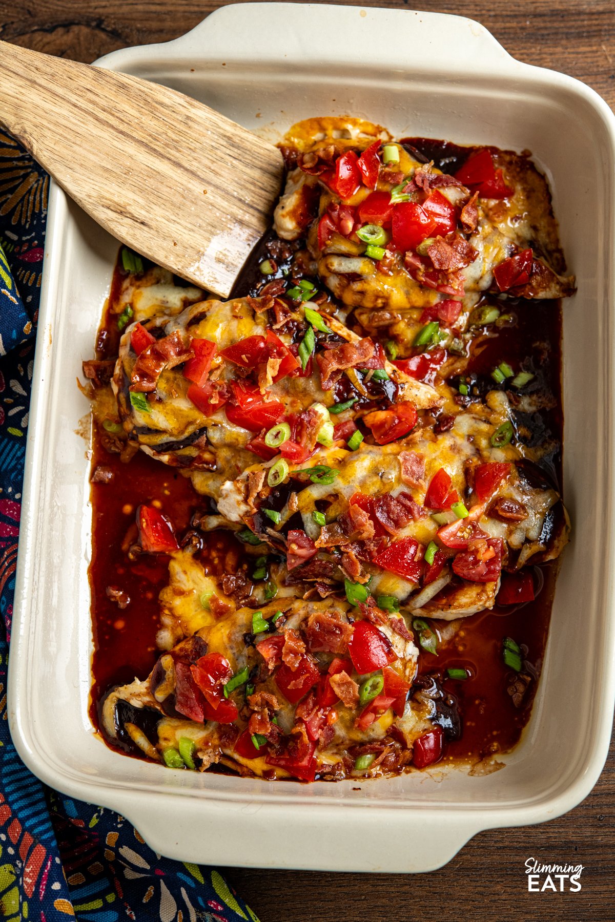 This easy Monterey Chicken is loaded with flavour, featuring tender chicken breasts topped with smoky BBQ sauce, melted cheese, fresh tomatoes and crispy bacon for a fuss-free dinner the whole family will love. 4 cooked Monterey style Chicken breasts in a oven dish with wooden spatula
