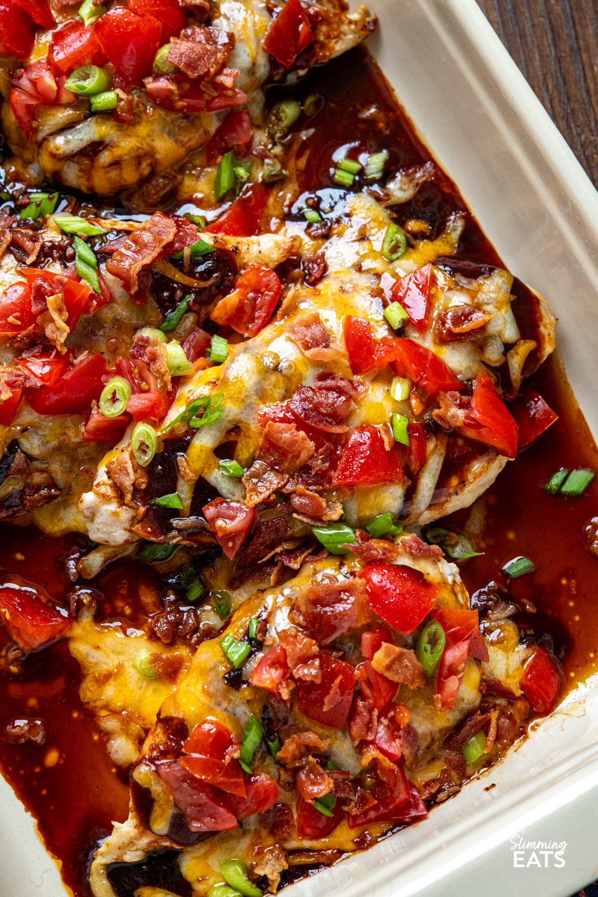 This easy Monterey Chicken is loaded with flavour, featuring tender chicken breasts topped with smoky BBQ sauce, melted cheese, fresh tomatoes and crispy bacon for a fuss-free dinner the whole family will love. close up of cooked Monterey style Chicken breasts in a oven dish with wooden spatula