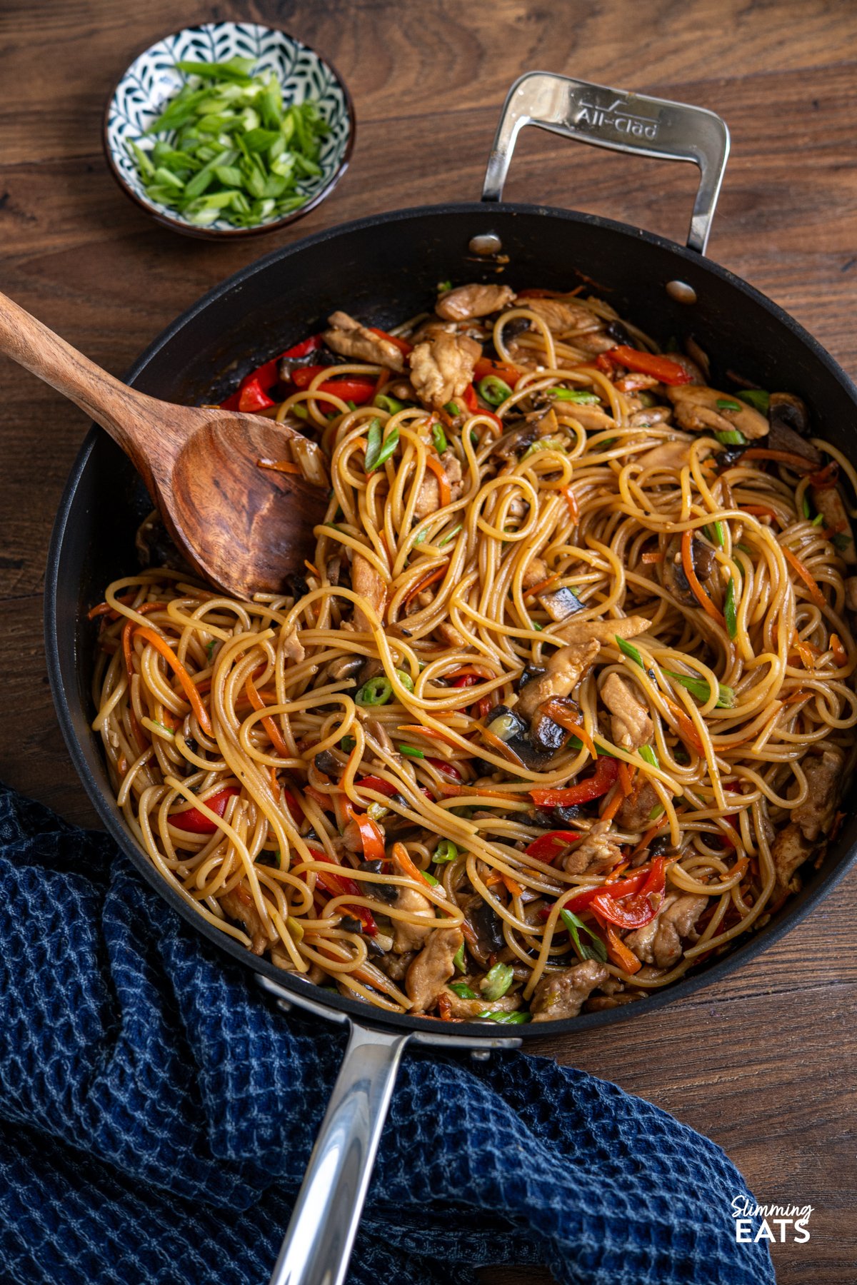 Say hello to your new weeknight favourite: One Pot Asian Garlic Chicken Noodles. This is everything you want from a quick noodle dish: tender chunks of chicken, loads of garlicky flavour, and a glossy, savoury sauce that clings to every strand of spaghetti. Yes, spaghetti! It might not be traditional, but it works perfectly in this one pot recipe, soaking up all those bold, punchy flavours without the fuss of boiling separately. Minimal effort, maximum flavour, and hardly any washing up. one pot garlic chicken noodles made with spaghetti in a all-clad non stick pan next to a blue kitchen towel.