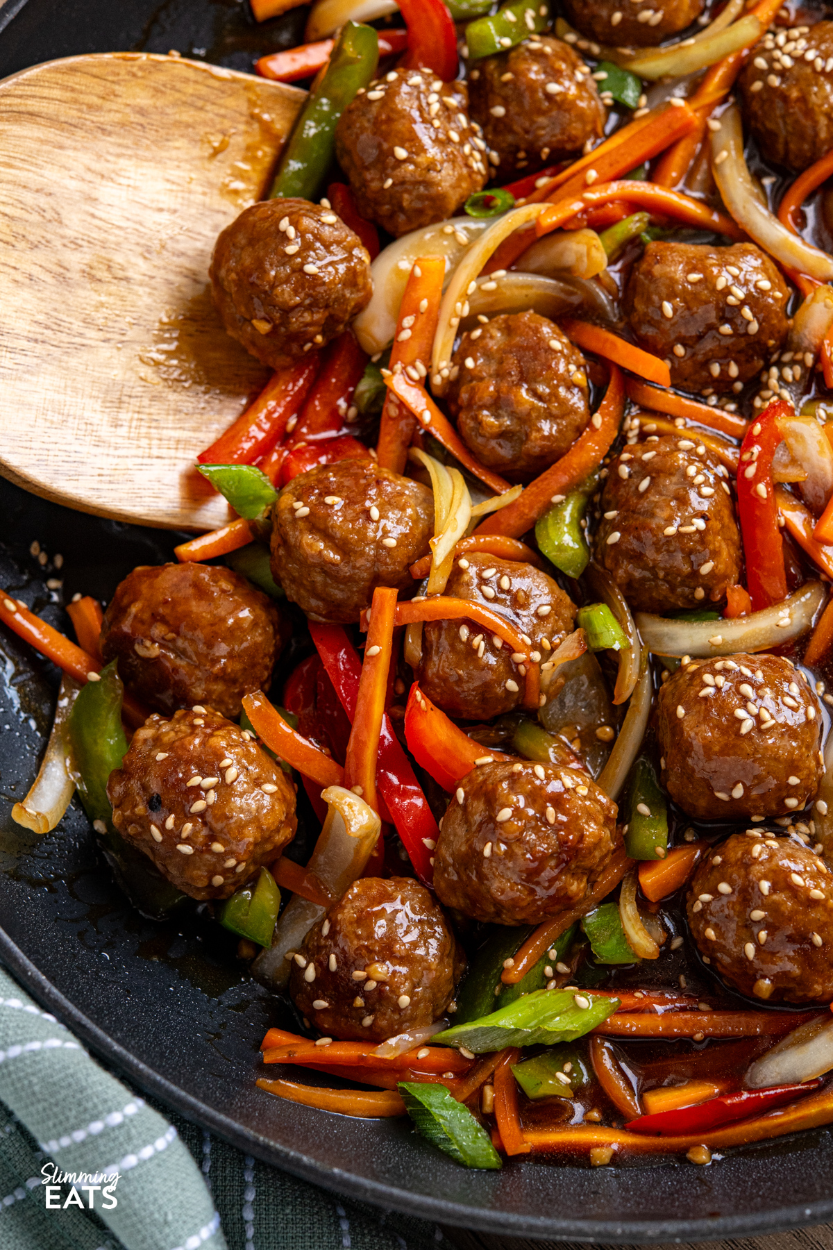 This Easy Asian Meatball Stir Fry is a quick and flavourful weeknight dinner that brings tender meatballs and vibrant vegetables together in a glossy savoury sweet sauce. close up of Easy Asian Meatball Stir Fry in frying pan with wooden spatula