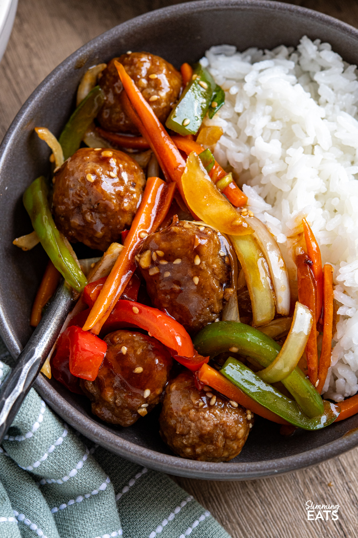 This Easy Asian Meatball Stir Fry is a quick and flavourful weeknight dinner that brings tender meatballs and vibrant vegetables together in a glossy savoury sweet sauce. close up of Easy Asian Meatball Stir Fry in grey bowl with rice