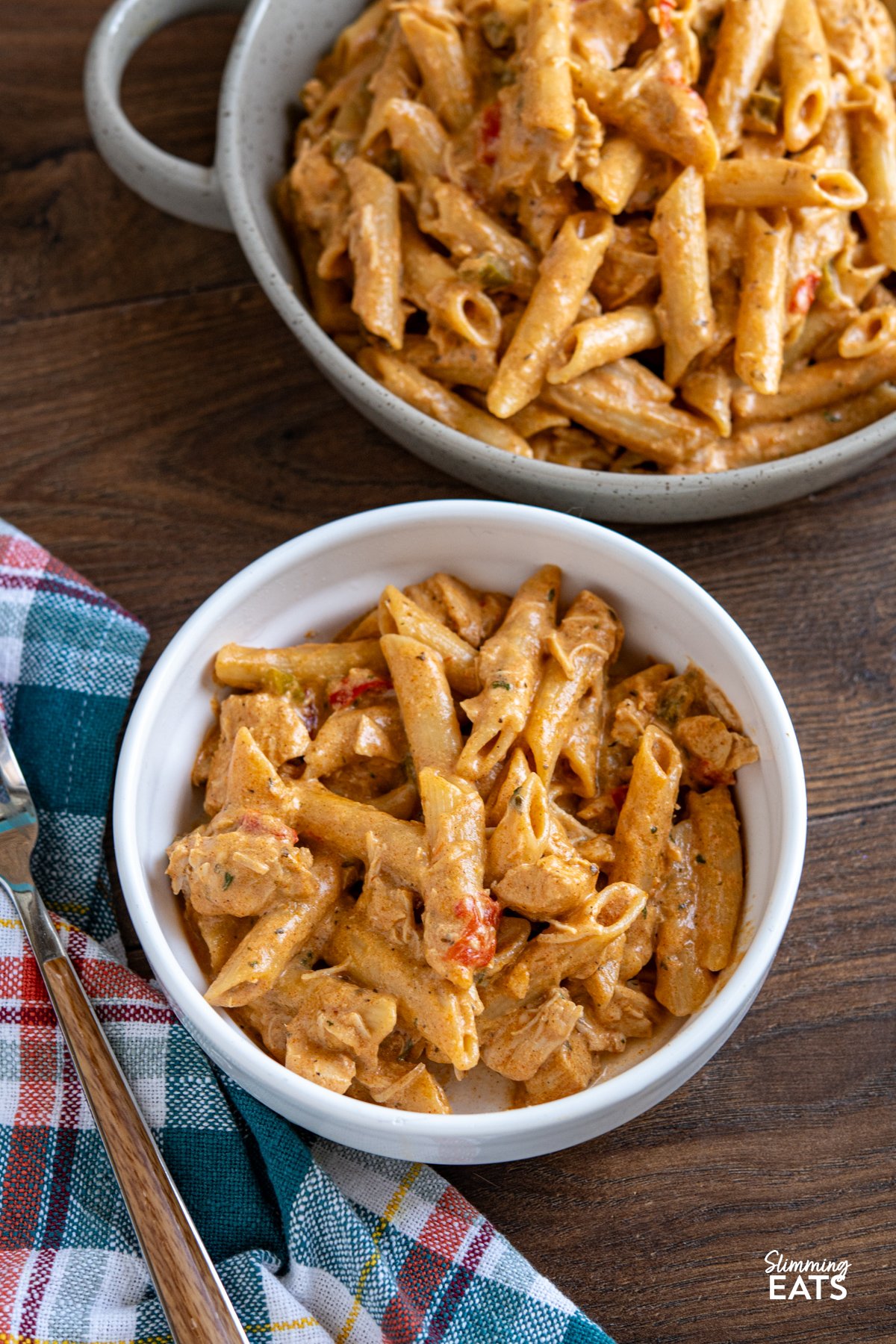 Slow Cooker Creamy Cajun Chicken Pasta is an easy, all-in-one meal with tender chicken, a light creamy sauce, and pasta cooked right in the slow cooker. Slow Cooker Creamy Cajun Chicken Pasta served in a white bowl with fork in bowl and blue, red, white, and yellow chequered kitchen towel to the left.