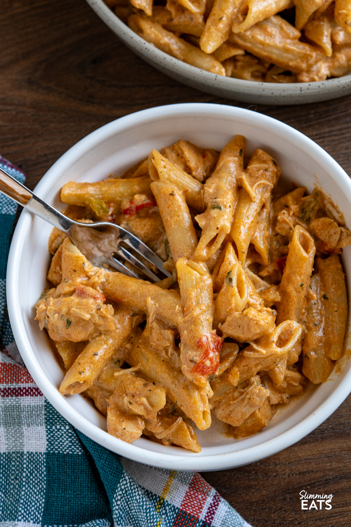 Slow Cooker Creamy Cajun Chicken Pasta is an easy, all-in-one meal with tender chicken, a light creamy sauce, and pasta cooked right in the slow cooker. Slow Cooker Creamy Cajun Chicken Pasta served in a white bowl with fork in bowl and blue, red, white, and yellow chequered kitchen towel to the left.