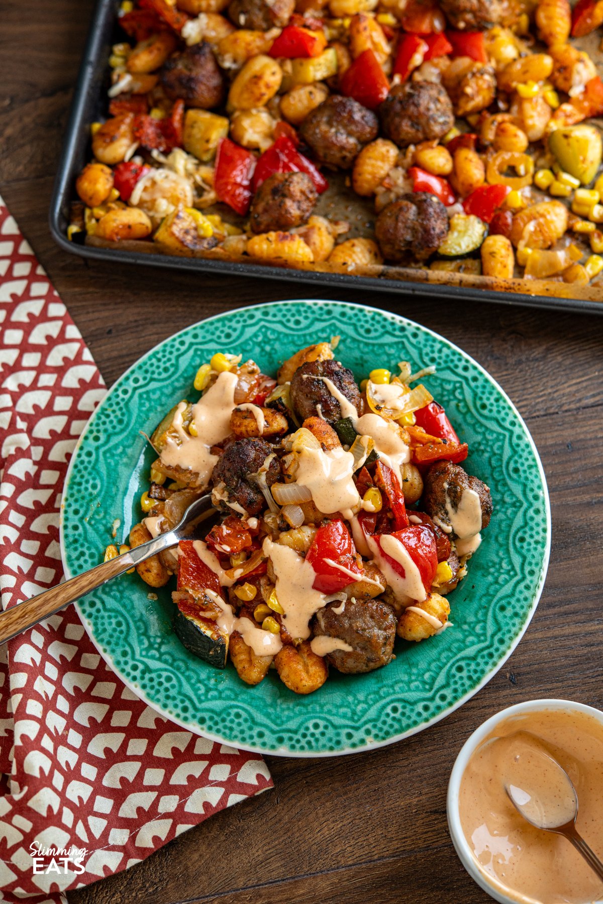 serving of Sausage Meatballs with Gnocchi on green teal plate with fork, drizzled with spicy mayo