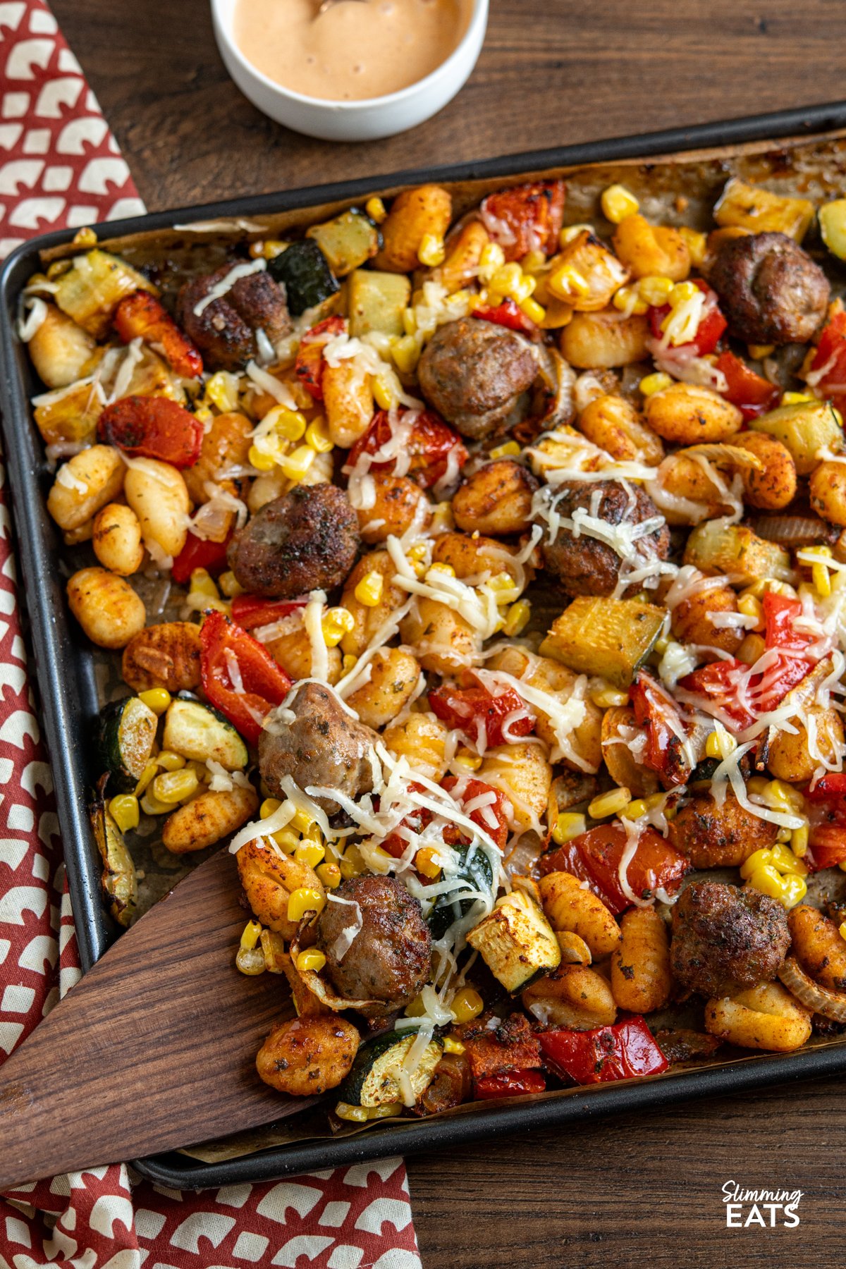 Sausage Meatballs with Gnocchi on baking tray lined with parchment with wooden spatula and side bowl of spicy mayo