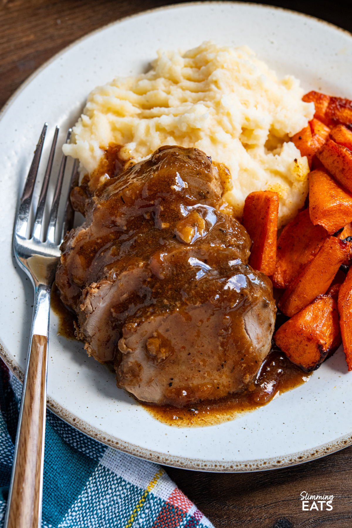close up of Slow Cooker Honey Soy Balsamic Pork Tenderloin on white plate with mashed potatoes and roasted carrots, fork placed on left of plate