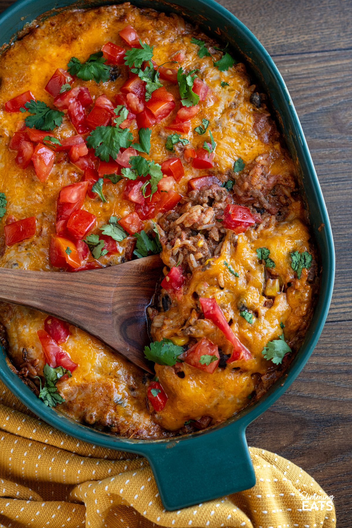 Enjoy all the flavours of a burrito in this easy Cheesy Beef Burrito Rice Bake packed with seasoned ground beef, fluffy rice, sweetcorn, black beans, and colourful peppers, every bite is full of Tex-Mex flair. close up of Cheesy Beef Burrito Rice Bake in dark green oven dish