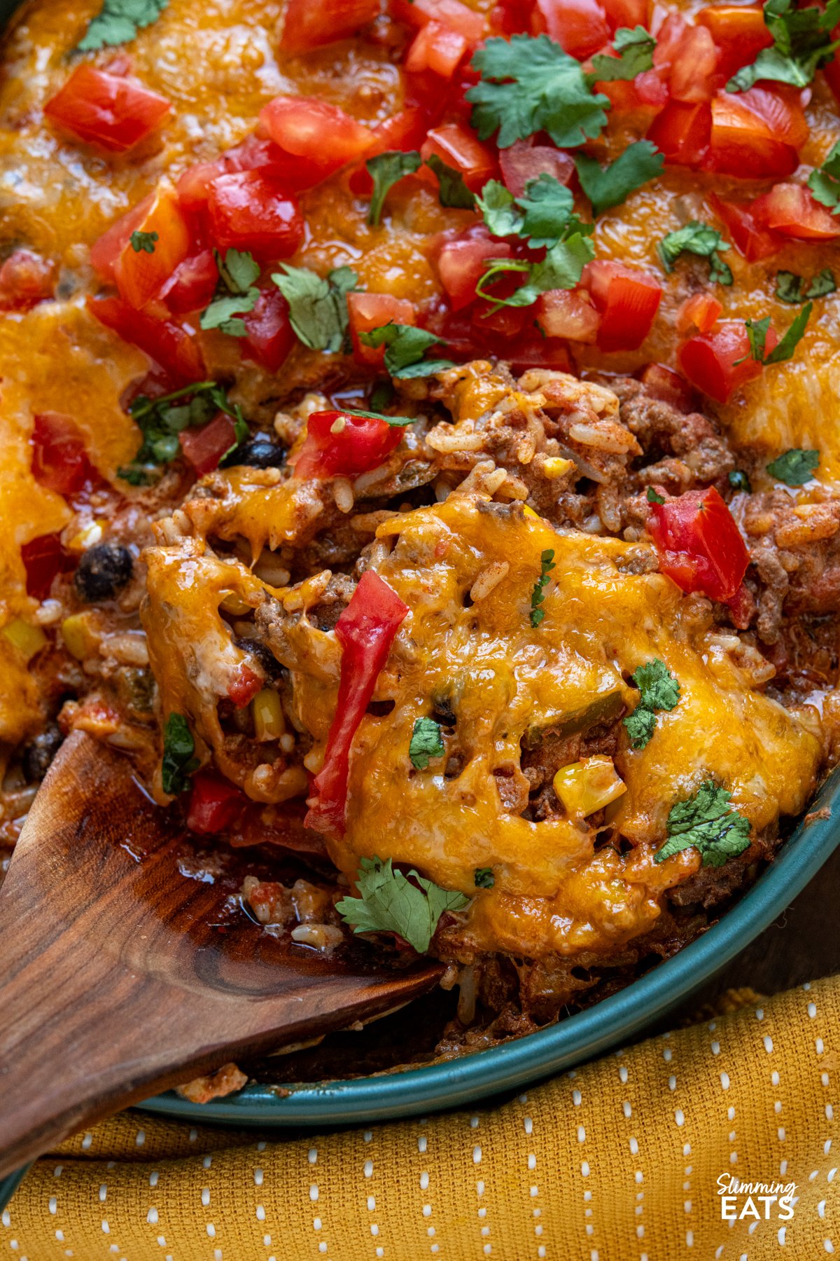 Enjoy all the flavours of a burrito in this easy Cheesy Beef Burrito Rice Bake packed with seasoned ground beef, fluffy rice, sweetcorn, black beans, and colourful peppers, every bite is full of Tex-Mex flair. close up of Cheesy Beef Burrito Rice Bake in dark green oven dish
