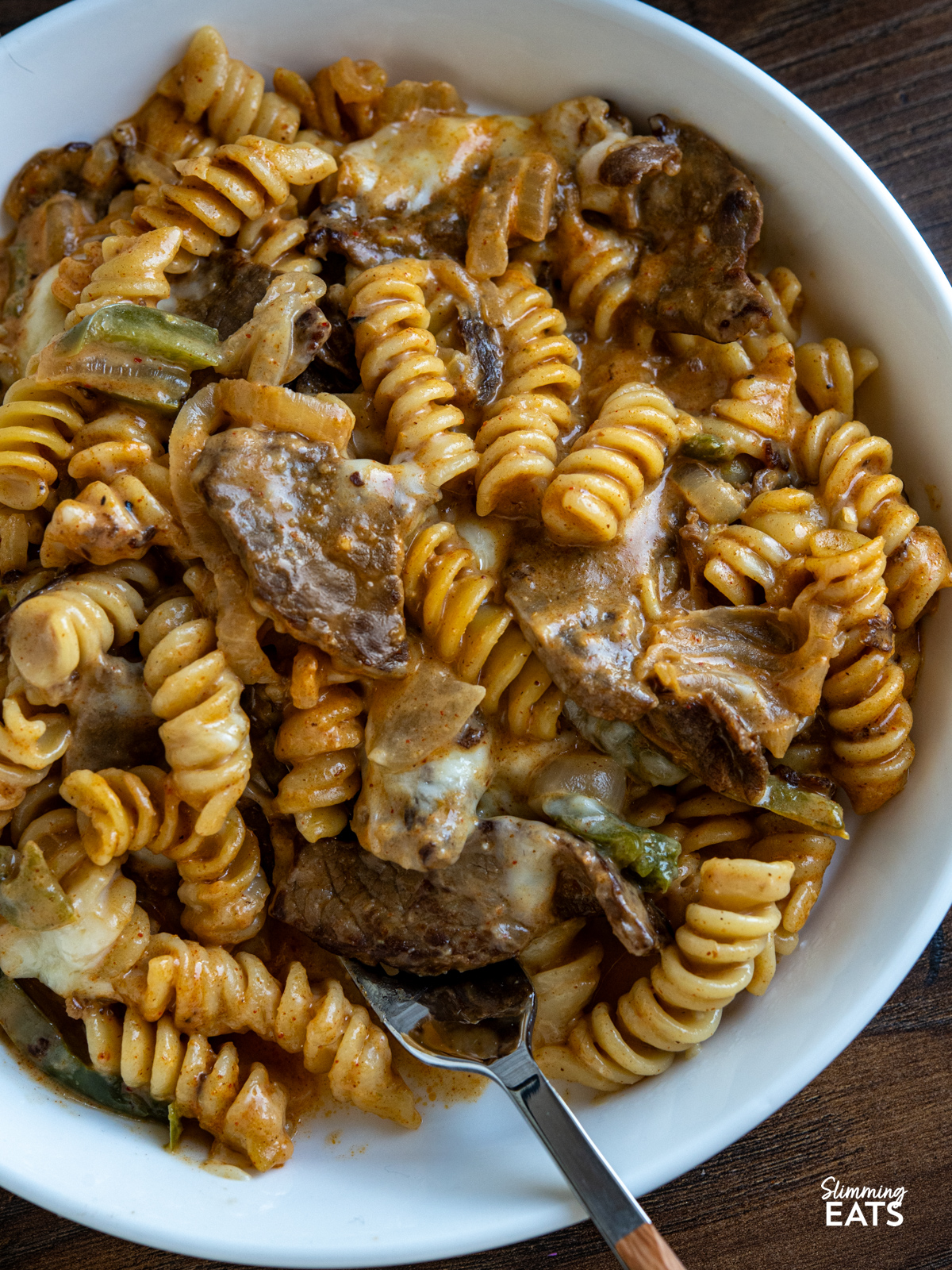 This One Pot Philly Cheesesteak Pasta is a creamy, cheesy twist on the classic sandwich, with tender beef, peppers, and onions all cooked together for an easy, comforting meal. close up of One Pot Philly Cheesesteak Pasta in white bowl with fork