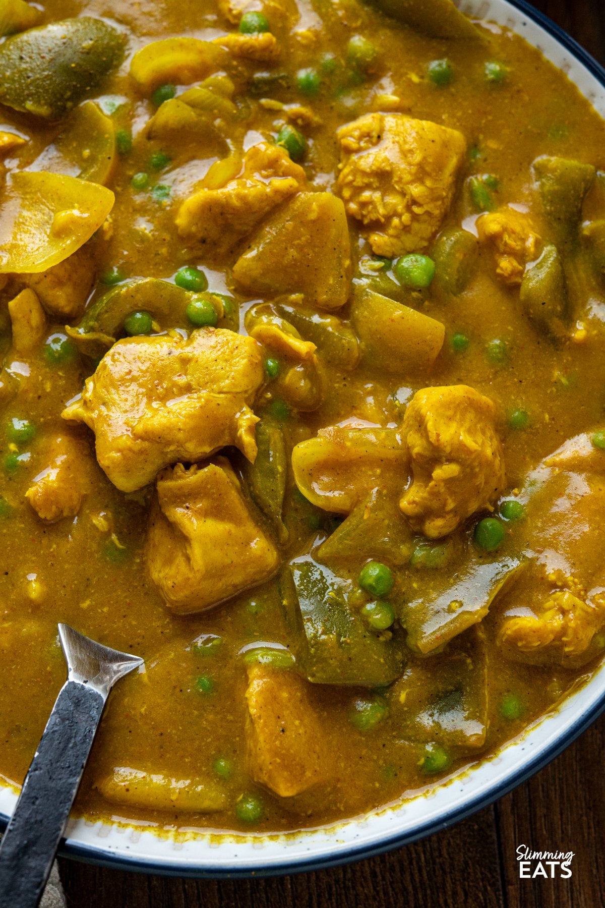 close up of Slow Cooker Chinese Chicken Curry in a large bowl with navy rim, serving spoon placed in bowl