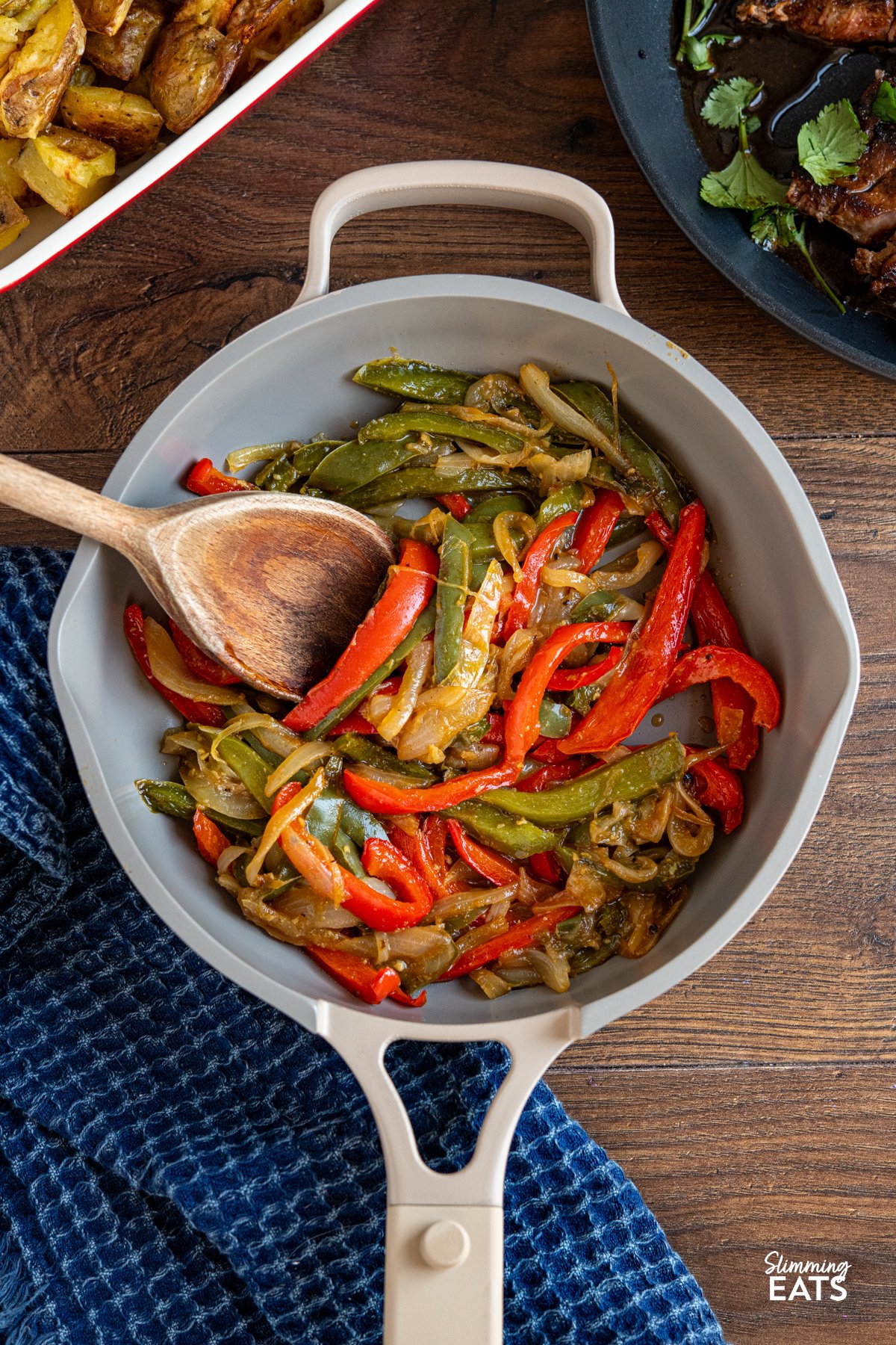 Simple, flavour packed sautéed peppers and onions cooked in stock for a tender, lightly caramelised side with minimal oil. Sauteed Peppers and Onions in a non stick frying pan with wooden spoon, sliced seasoned steak and peppers visible above